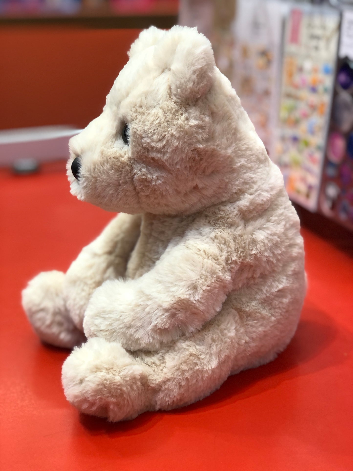 Soft, cuddly cream-colored teddy bear plush toy sitting on red surface, perfect for hugging and playtime
