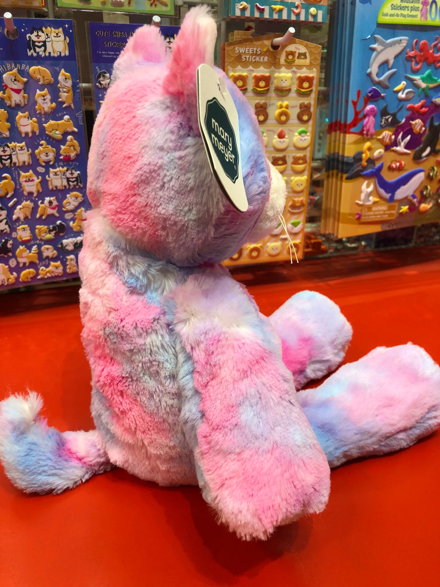 Soft pink Mary Meyer Marshmallow Cupcake Kitty plush toy displayed with colorful sticker sets in toy store