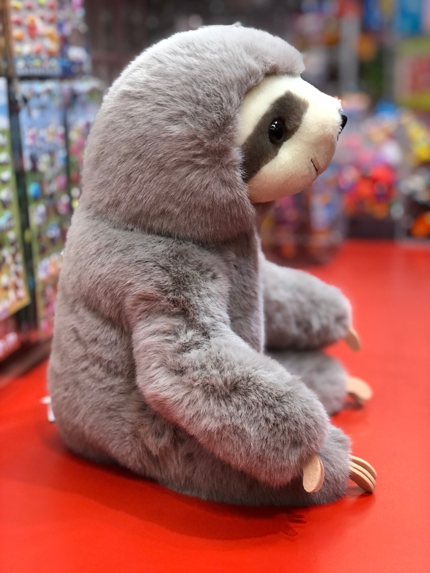 Cuddly Douglas Super Lizzie Soft Sloth plush toy with lifelike features, sitting on red surface in toy store display
