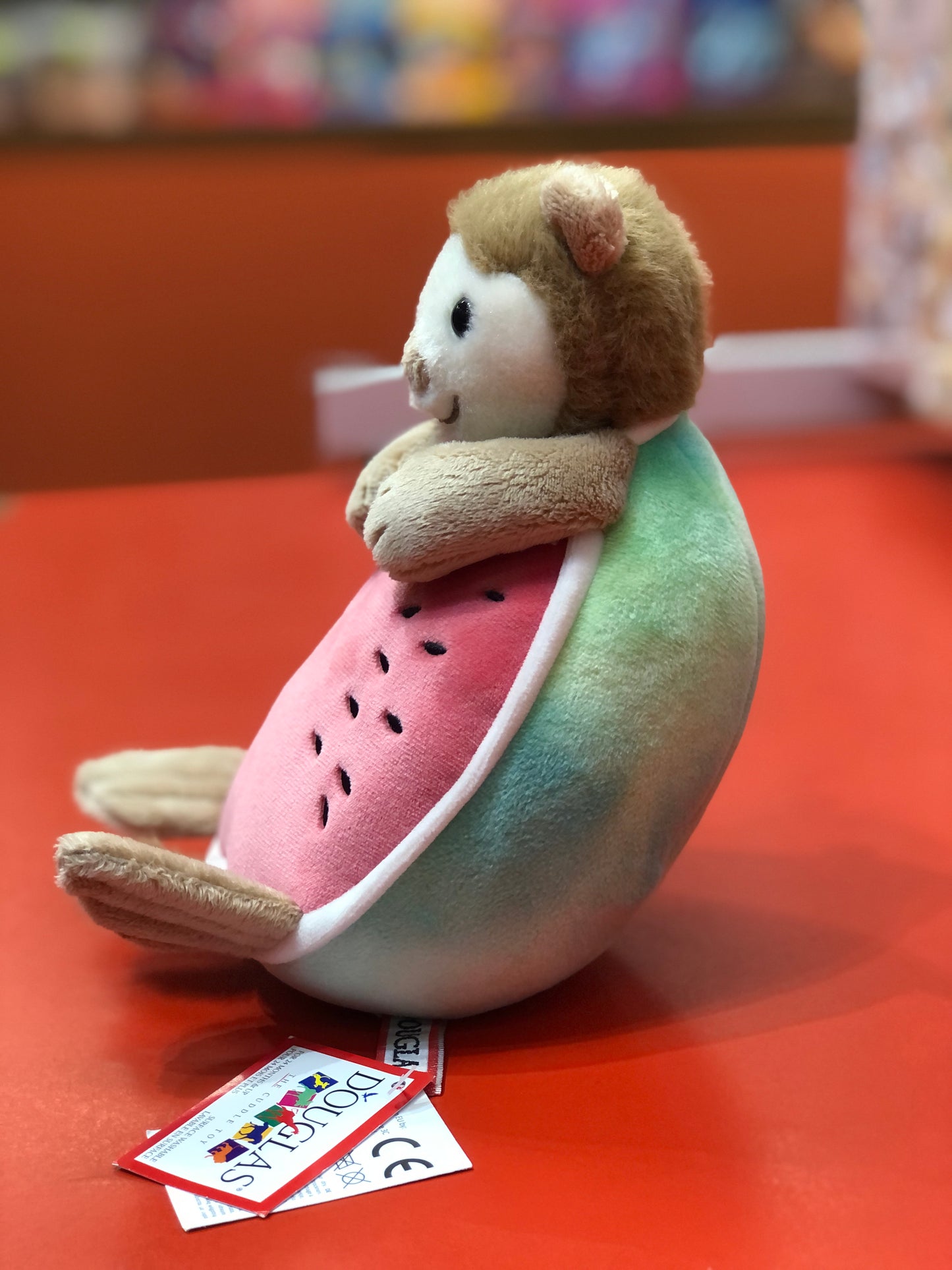 Cute Douglas Otter Melon plush toy, combining otter and watermelon in whimsical design, sitting on red surface with product tags