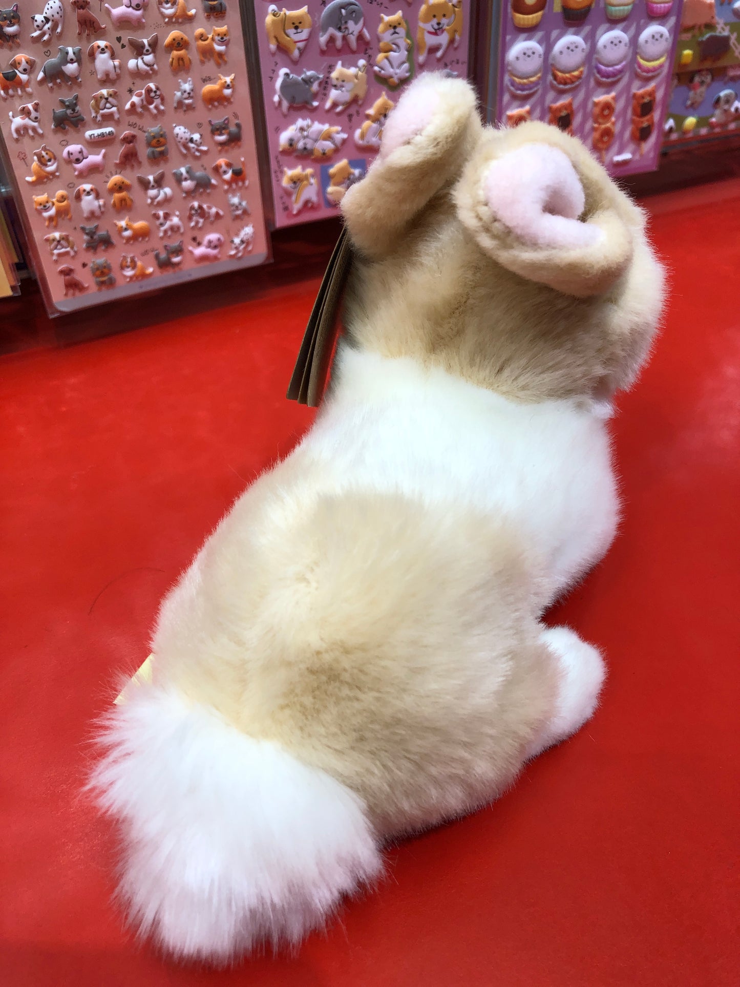 Soft ginger and white plush bunny toy on red surface, with colorful animal stickers in background