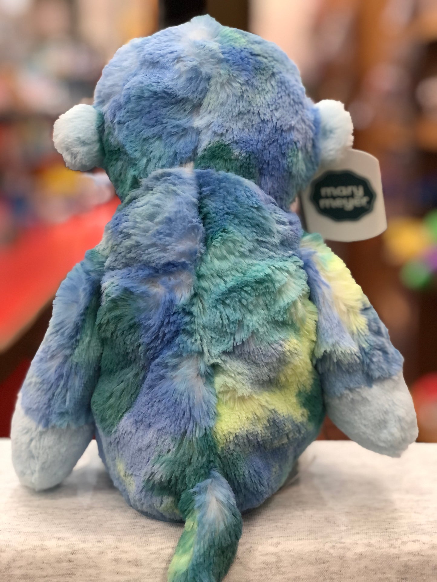 Soft, plush Mary Meyer Marshmallow Mojo Monkey in blue and green tones, viewed from behind, with tag visible
