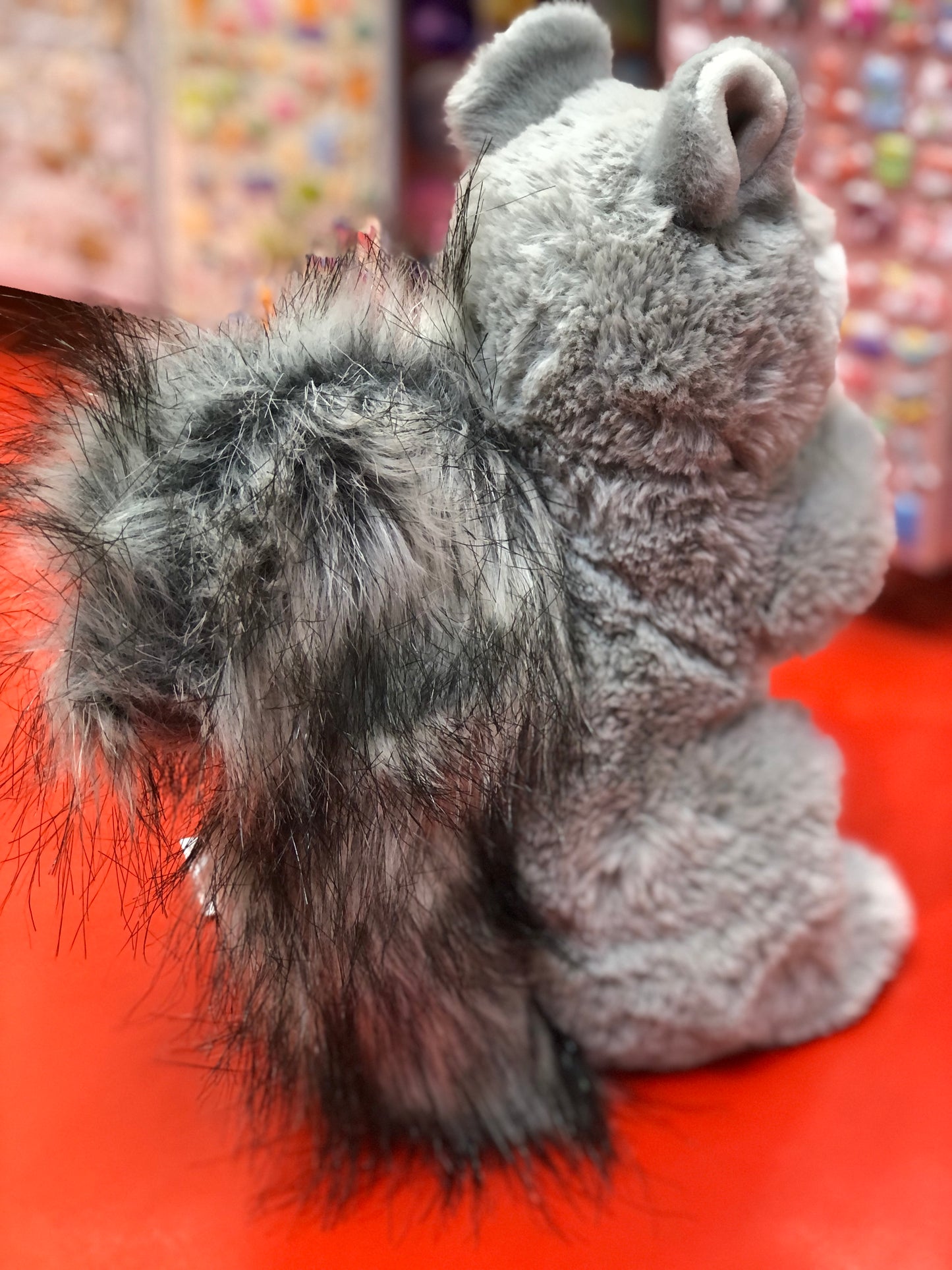 Soft plush gray squirrel toy with fluffy tail on red surface, showcasing Douglas Swiftie's lifelike details and cuddly texture