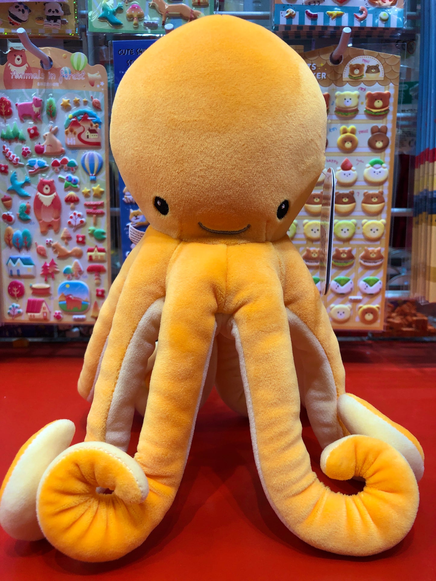Soft yellow Mary Meyer Smootheez Octopus plush toy with embroidered face, displayed in toy store with colorful background