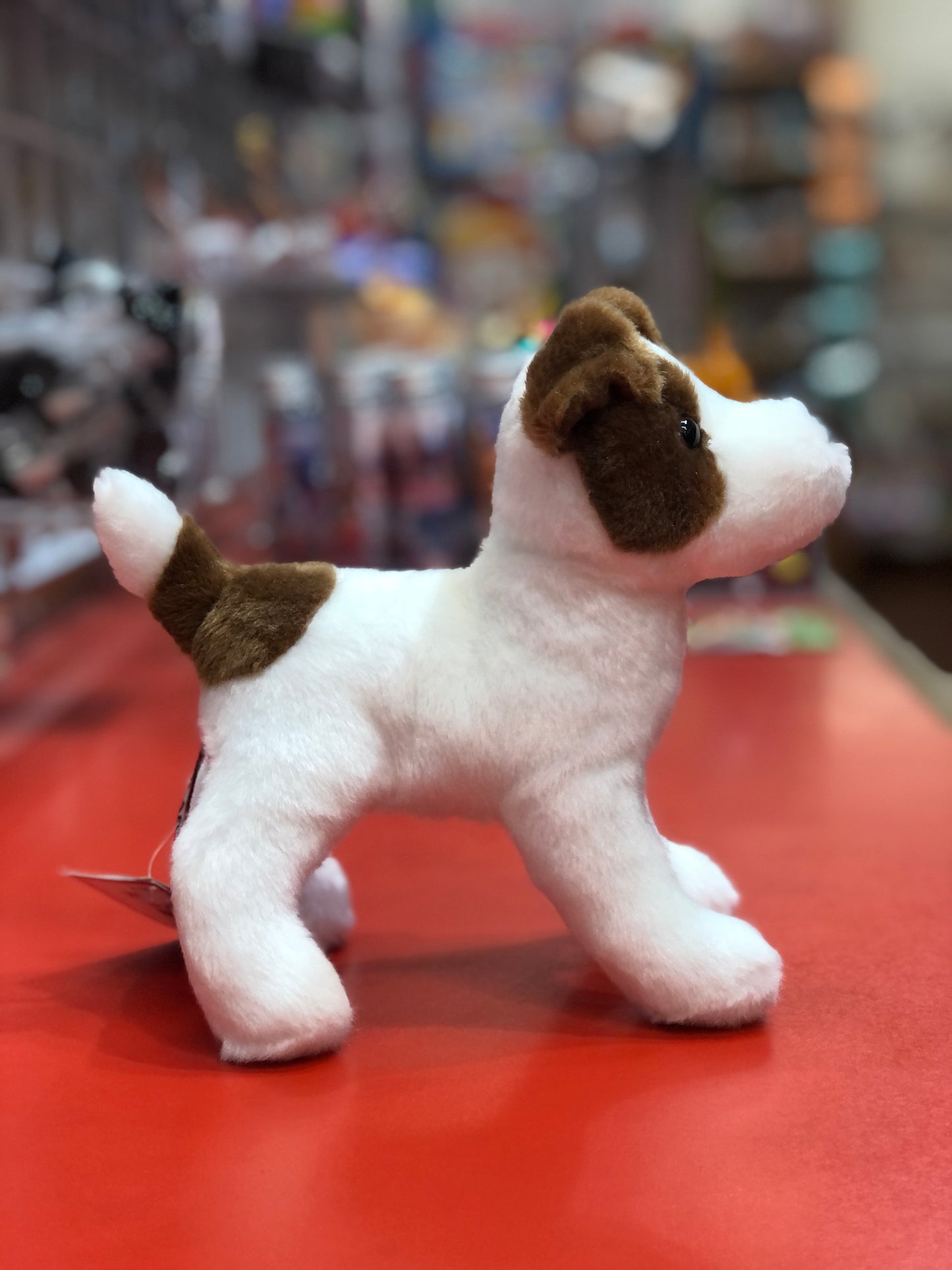 Cute Jack Russell plush toy with brown and white fur standing on red surface, showcasing playful and eager stance