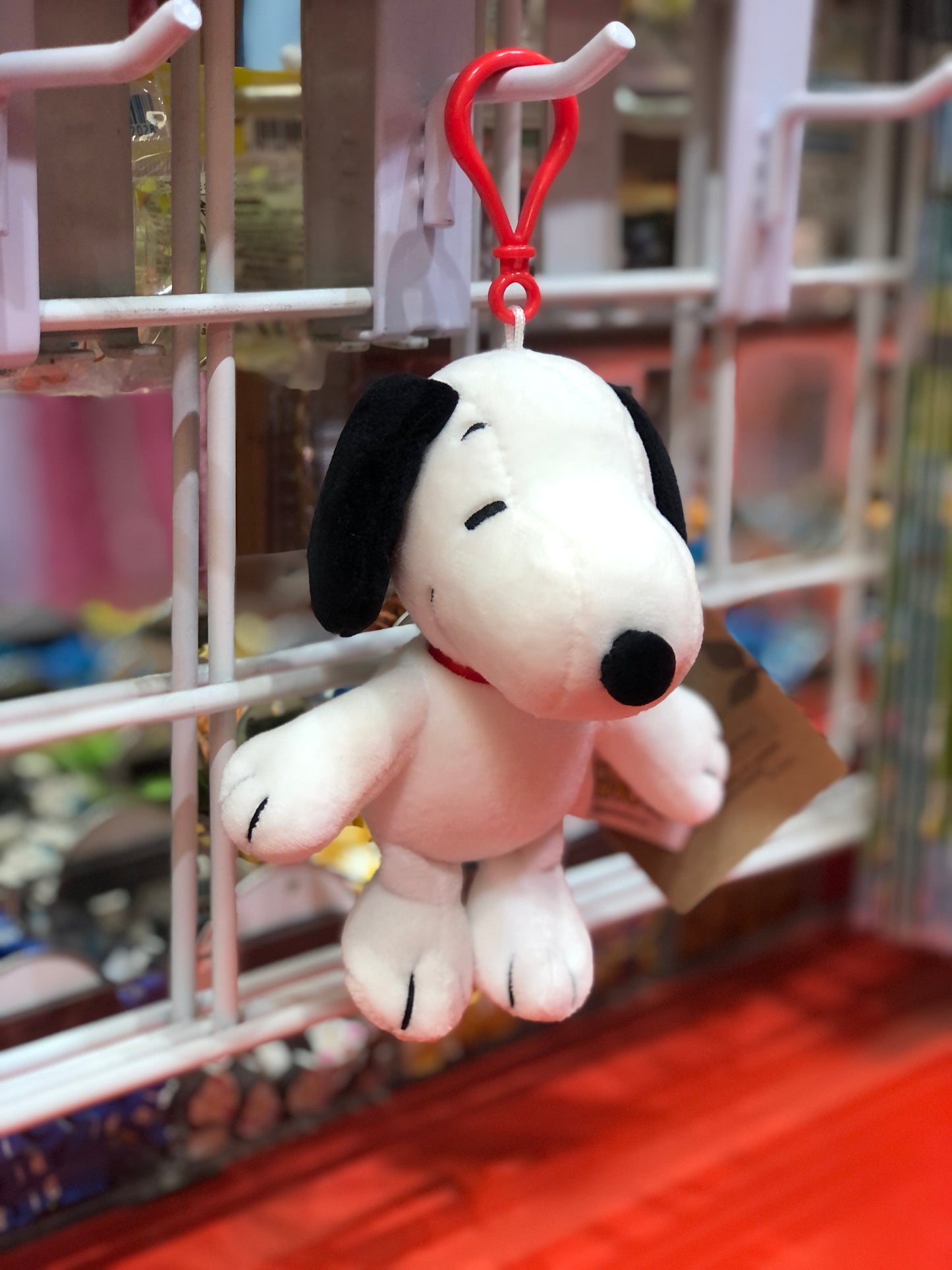 Adorable Snoopy plush keychain from Aurora's Peanuts collection, hanging on display in a toy store