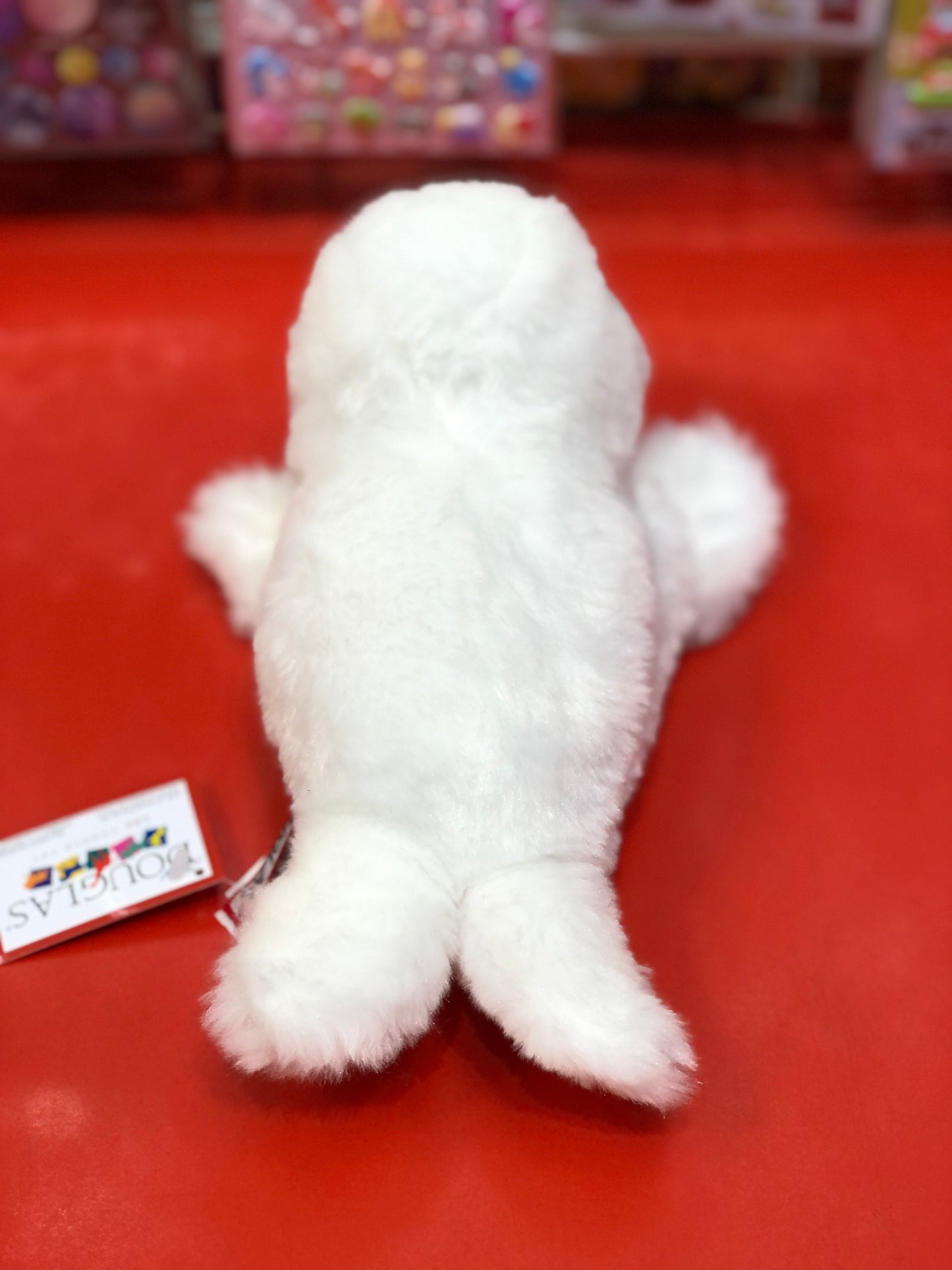 Soft white Sprinkles the Harp Seal plush toy on red surface, 9-inch huggable stuffed animal for ages 2+
