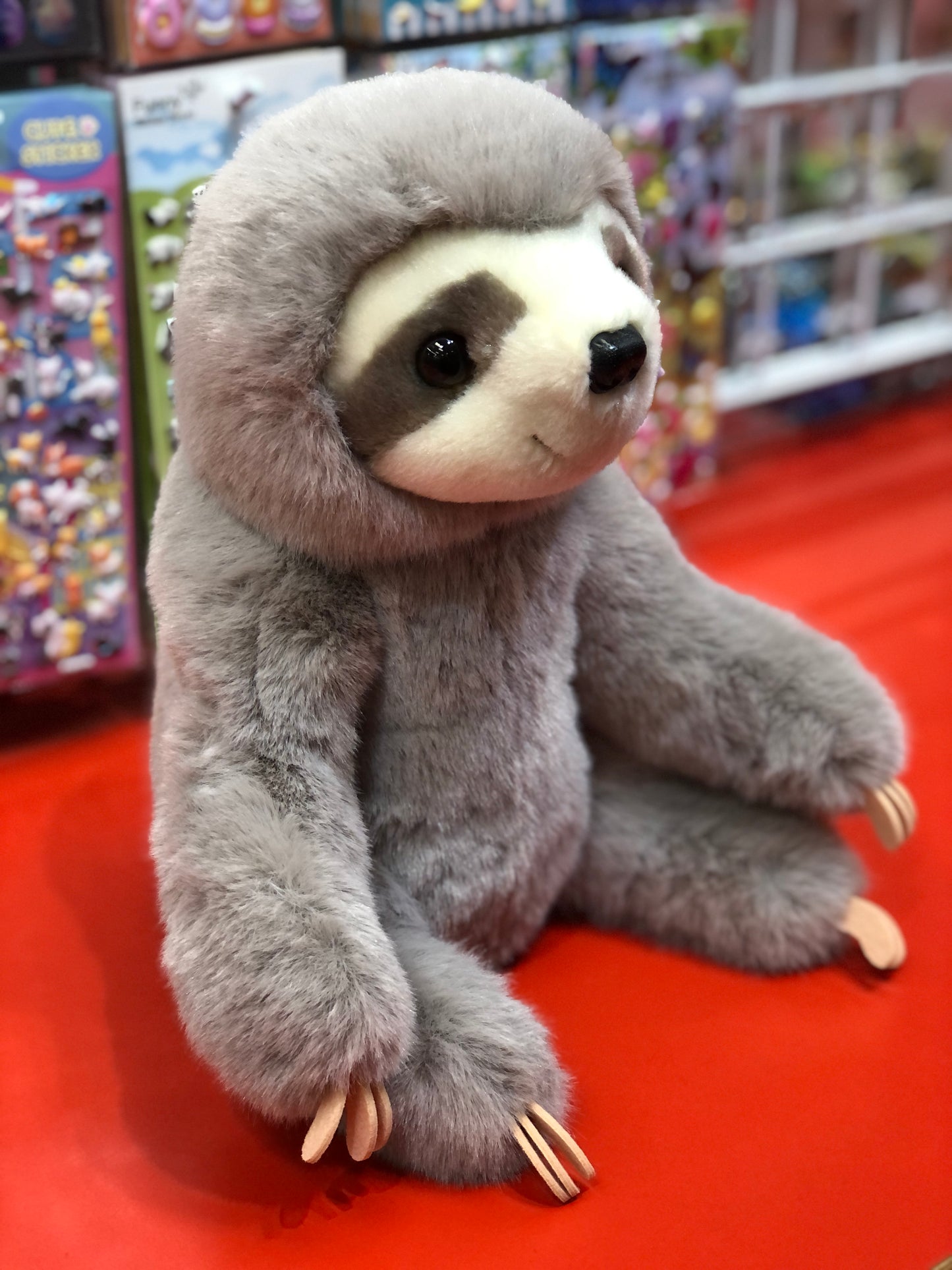 Cuddly Douglas Super Lizzie Soft Sloth plush toy with realistic features, sitting on red surface in toy store display