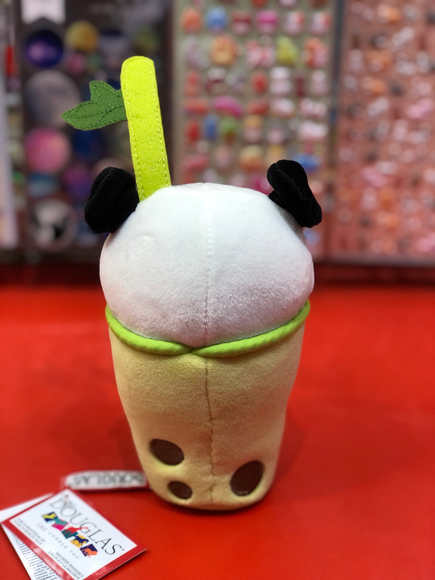 Cute panda bubble tea plush toy with soft white head, black ears, yellow cup, and green straw on red display shelf