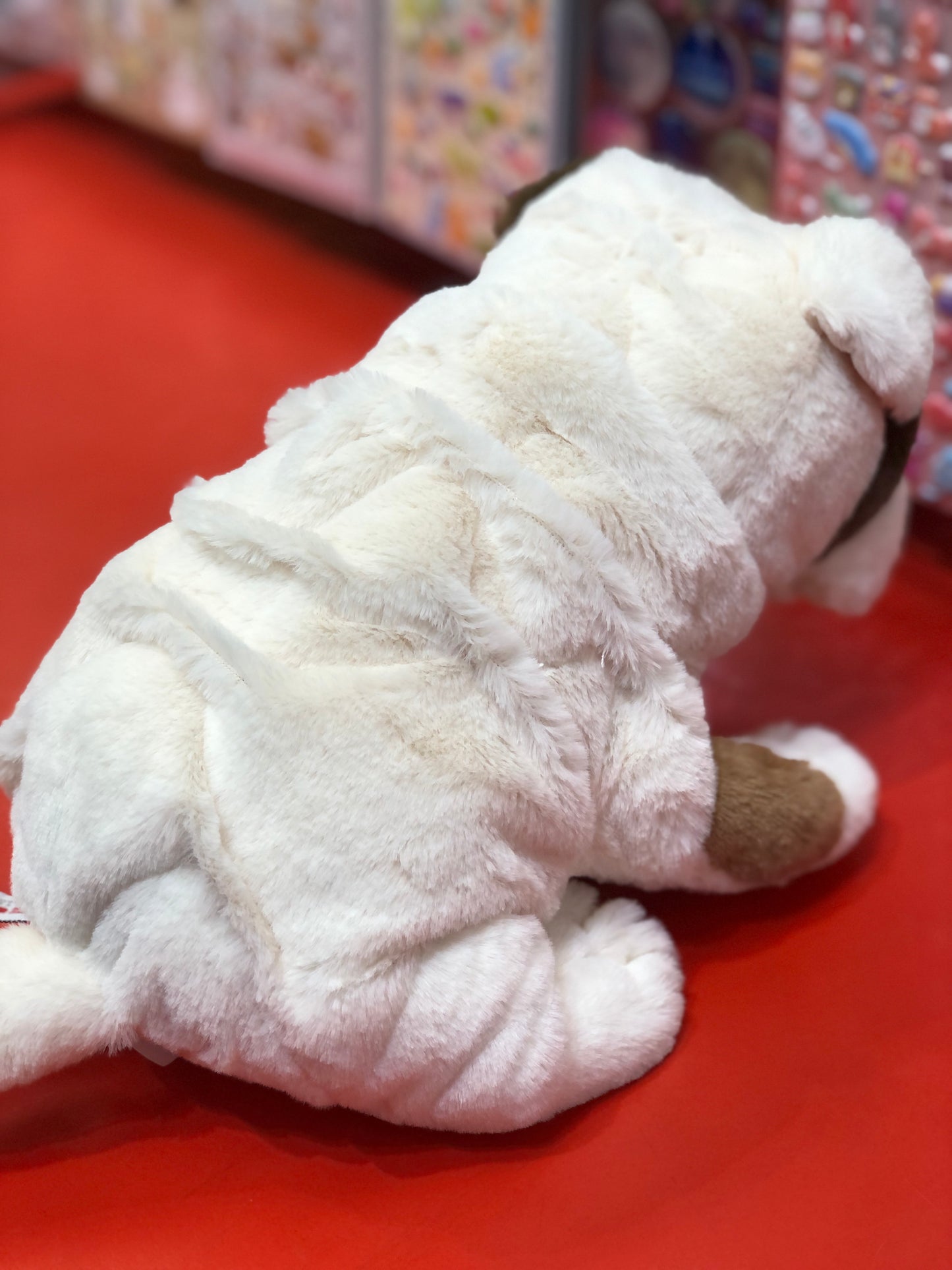 Gund Toast Bulldog plush toy sitting on red surface, cream-colored with wrinkled design, 10 inches long, realistic appearance
