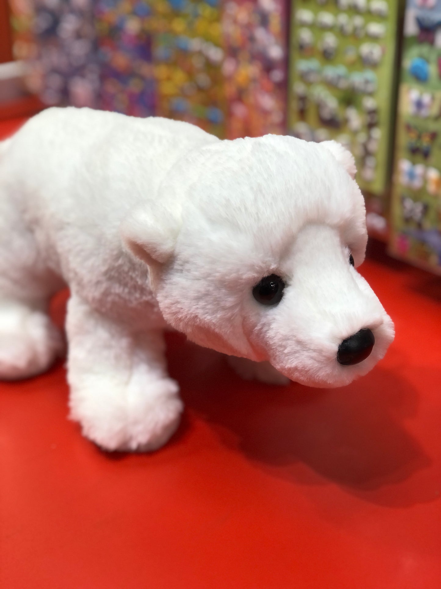 Soft white polar bear plush toy on red surface, realistic features, cuddly 9-inch Douglas Whitie stuffed animal