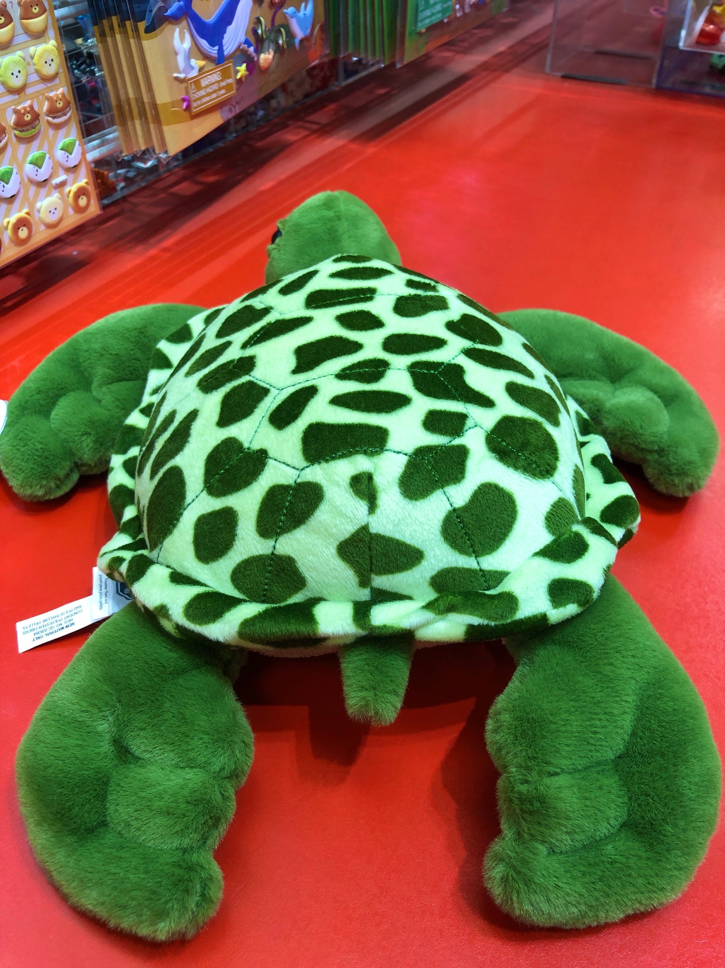 Plush green sea turtle toy with patterned shell on red display, showcasing Mary Meyer's 13-inch Ernie design