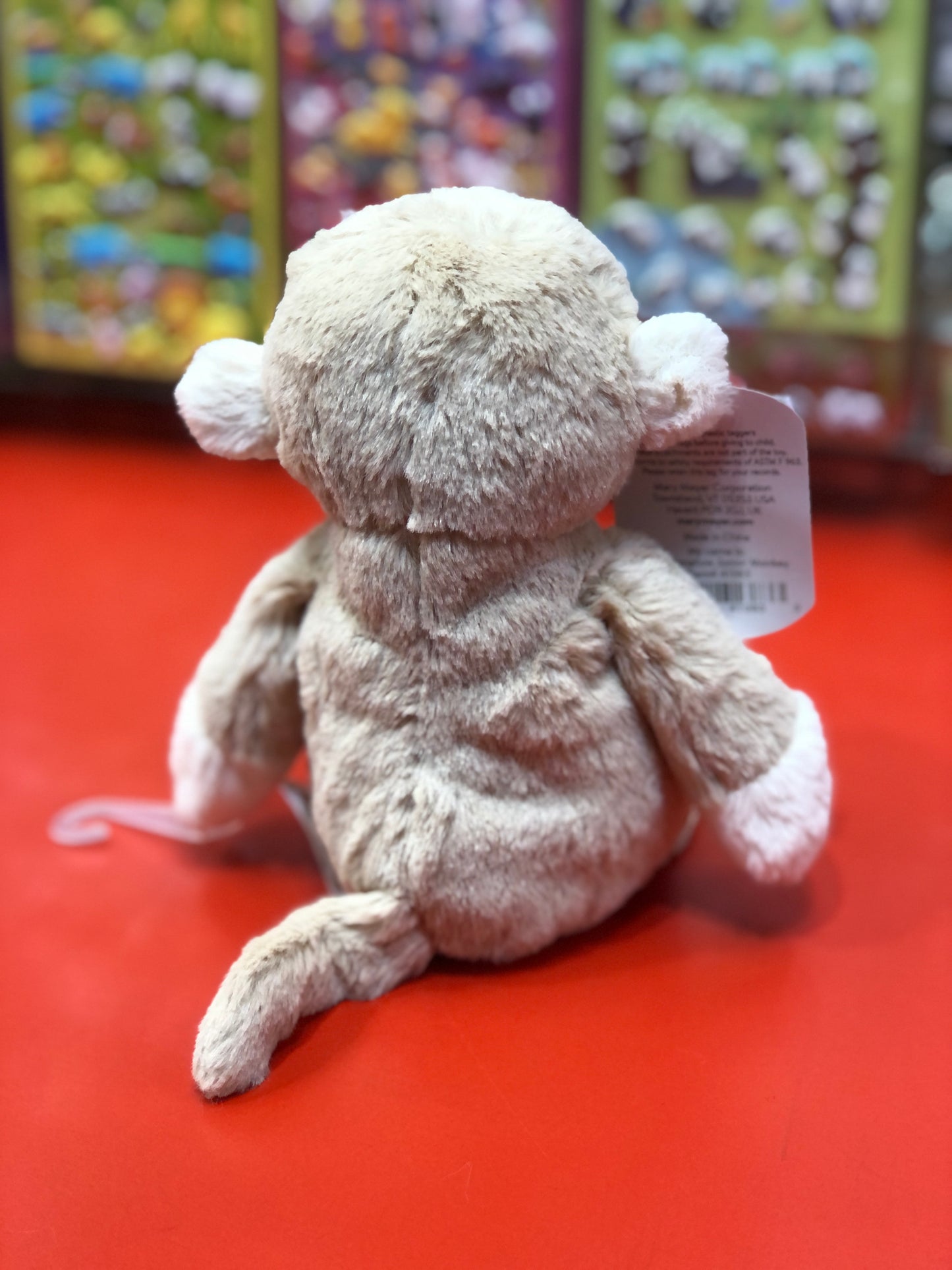 Soft, plush Mary Meyer Marshmallow Zoo monkey toy sitting on red surface, back view, with product tag visible