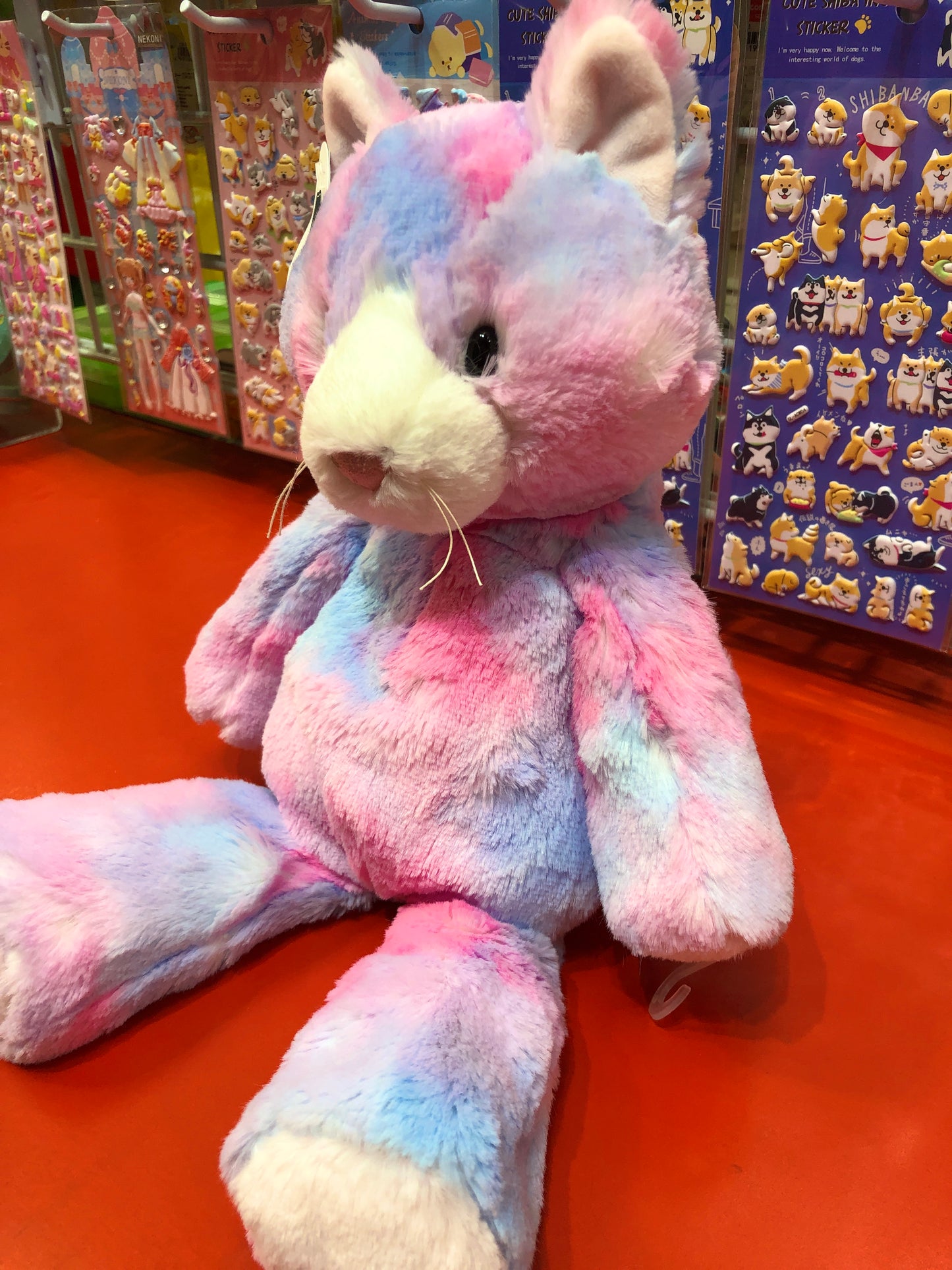 Soft pastel-colored Marshmallow Cupcake Kitty plush toy with embroidered features, displayed in toy store with sticker sheets behind