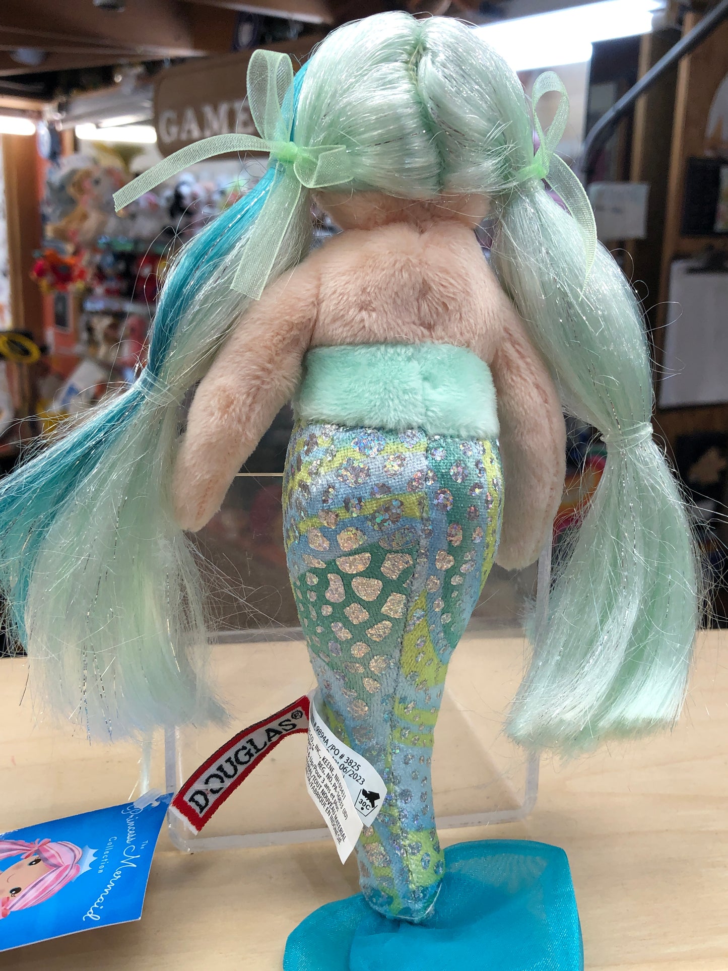 Douglas Princess Mermaid plush toy with pastel green hair, sparkly tail, and ribbon accents, displayed on store shelf