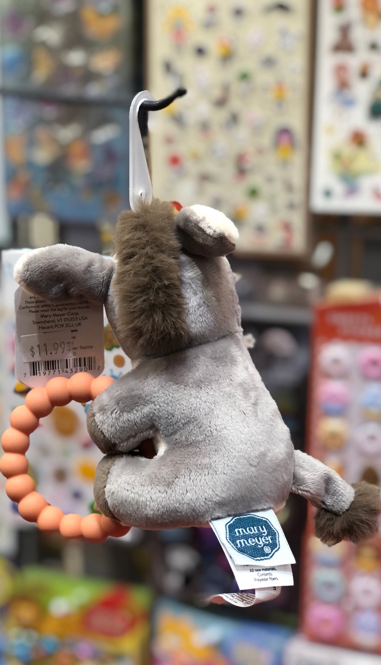 Soft plush donkey teether rattle toy with large ears, silicone ring, and Mary Meyer tag, displayed in colorful toy store setting