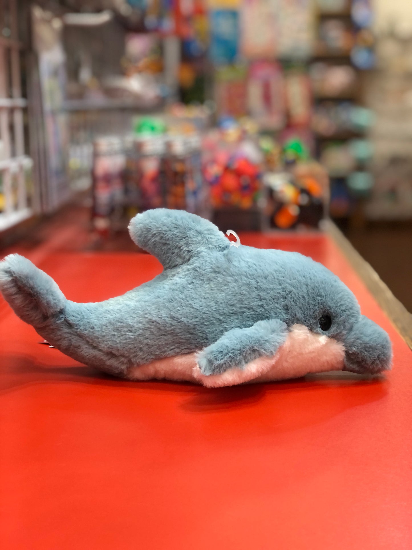 Soft blue dolphin plush toy on red surface, realistic features with pale underside, in colorful toy store display