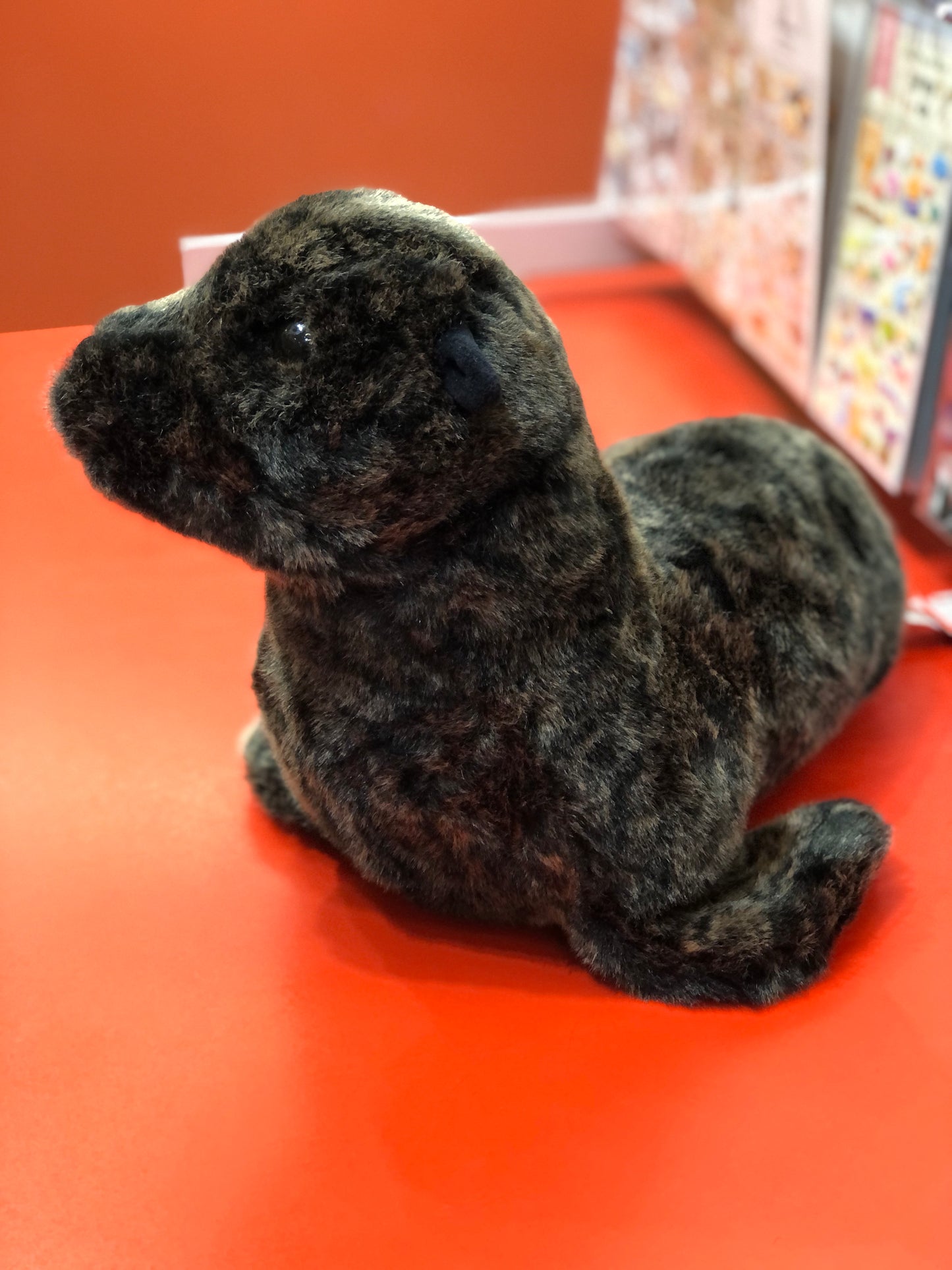 Soft, realistic Douglas Buoy sea lion plush toy on red surface, showcasing detailed fur and lifelike features