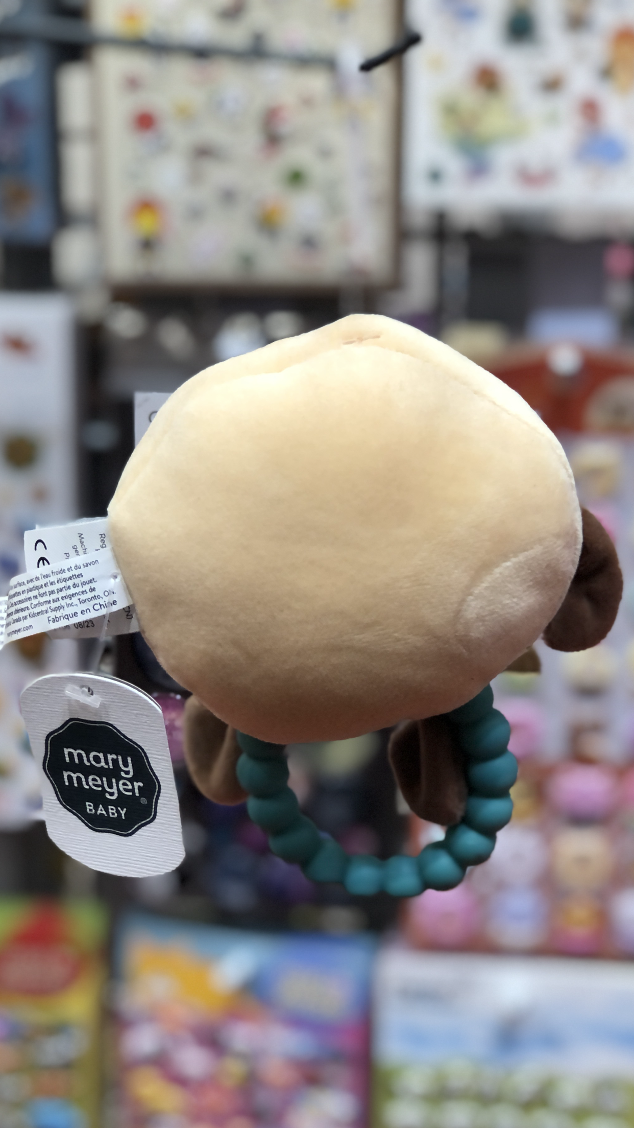 Mary Meyer Sweet Soothie Cookie teether rattle with soft plush top, teal ring, and brand tag against colorful toy display background