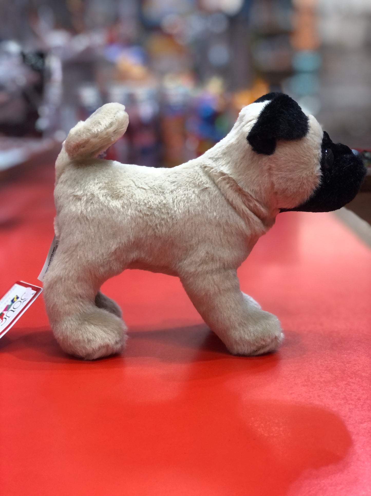 Douglas Hamilton 8" pug plush toy on red surface, realistic features with curly tail and wrinkled face, soft beige fur