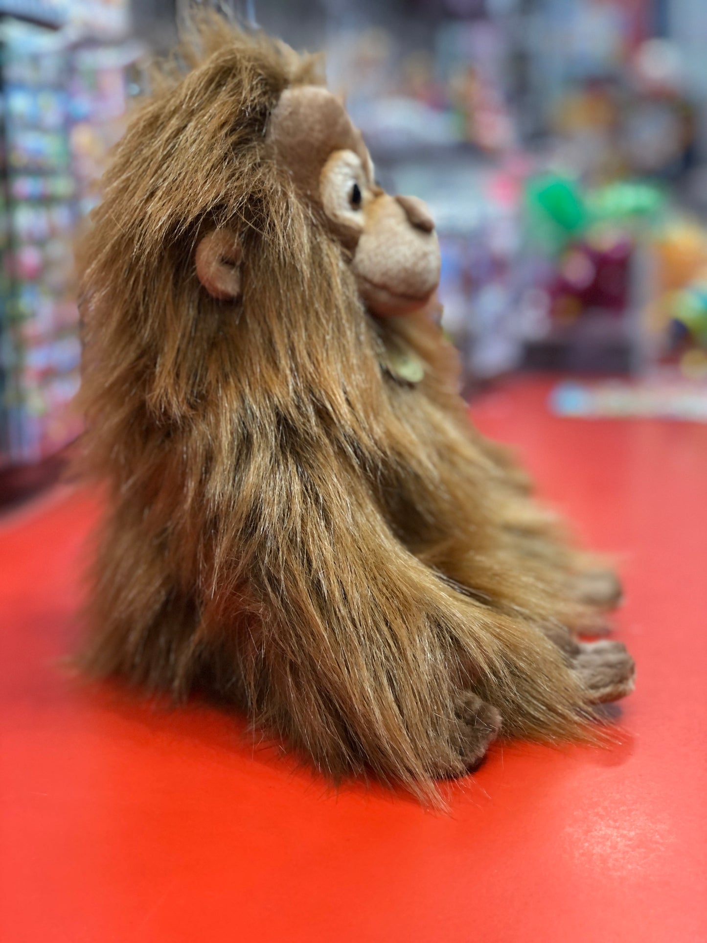 Adorable baby orangutan plush toy with realistic brown fur, sitting on red surface in toy store display