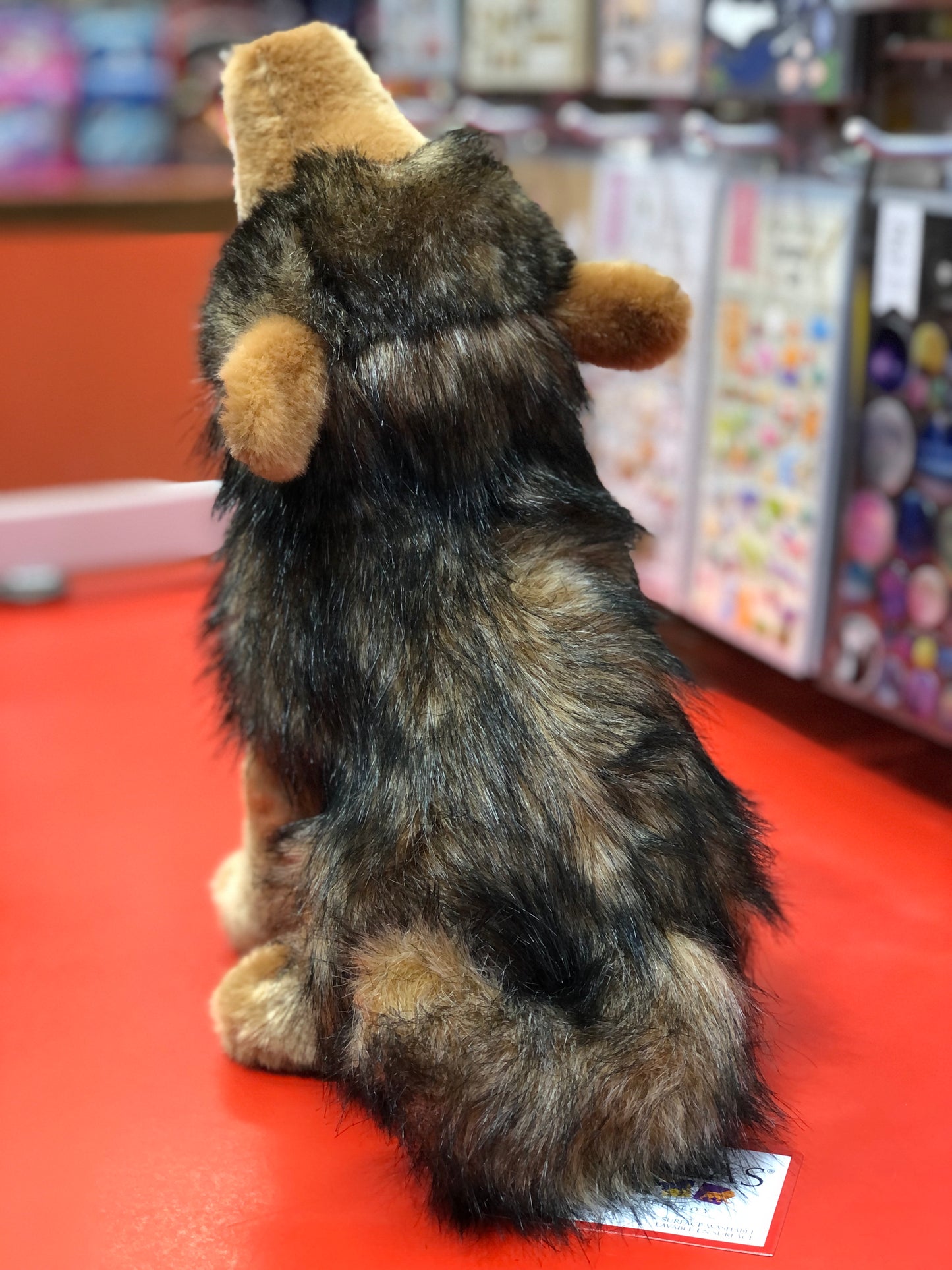 Realistic Douglas Rambler Coyote plush toy howling, with gray and brown fur, sitting on red surface in store display