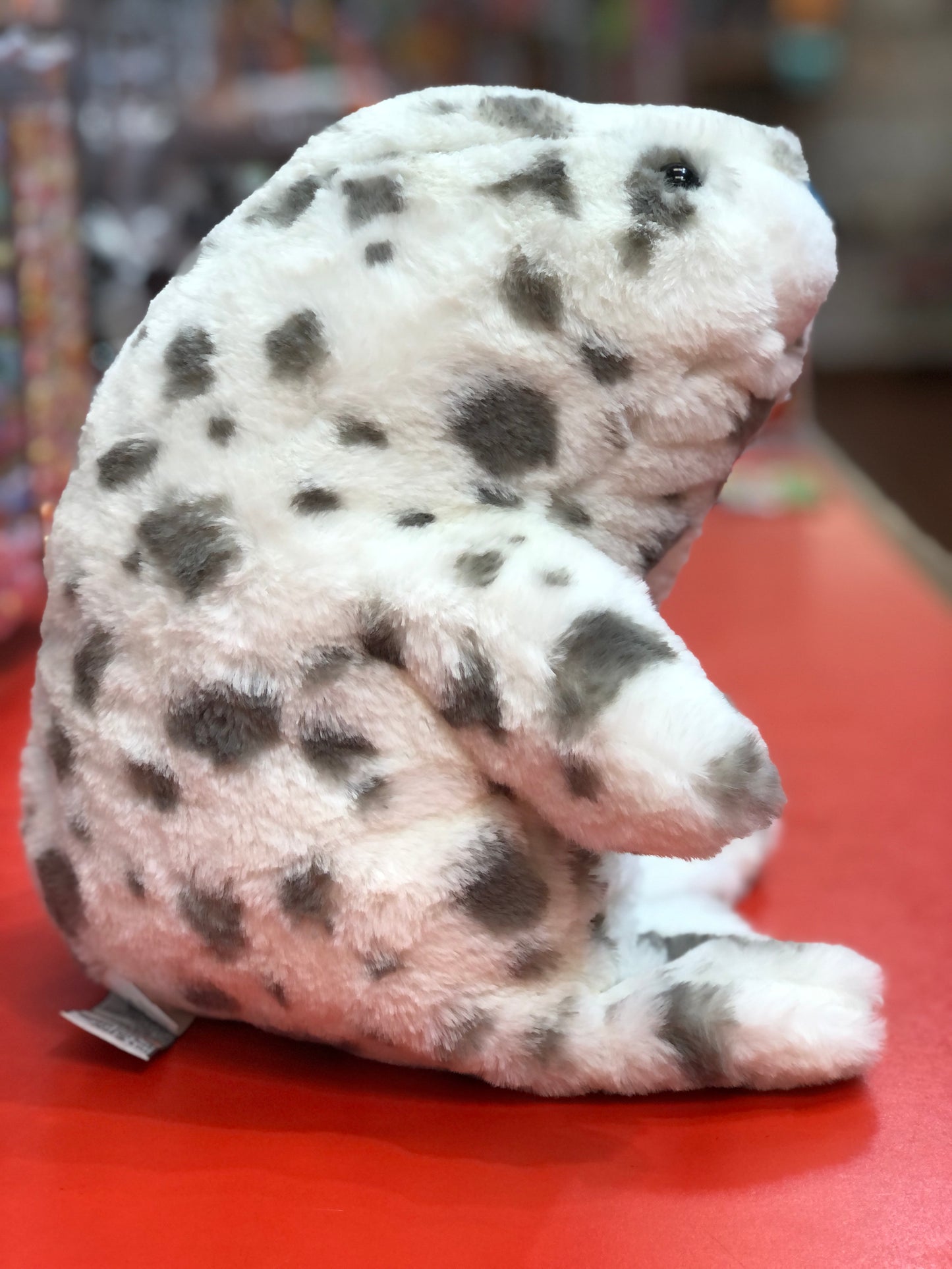 Soft Gund Nuri leopard seal plush toy with white and gray spotted design, curved shape for hugging, on red surface