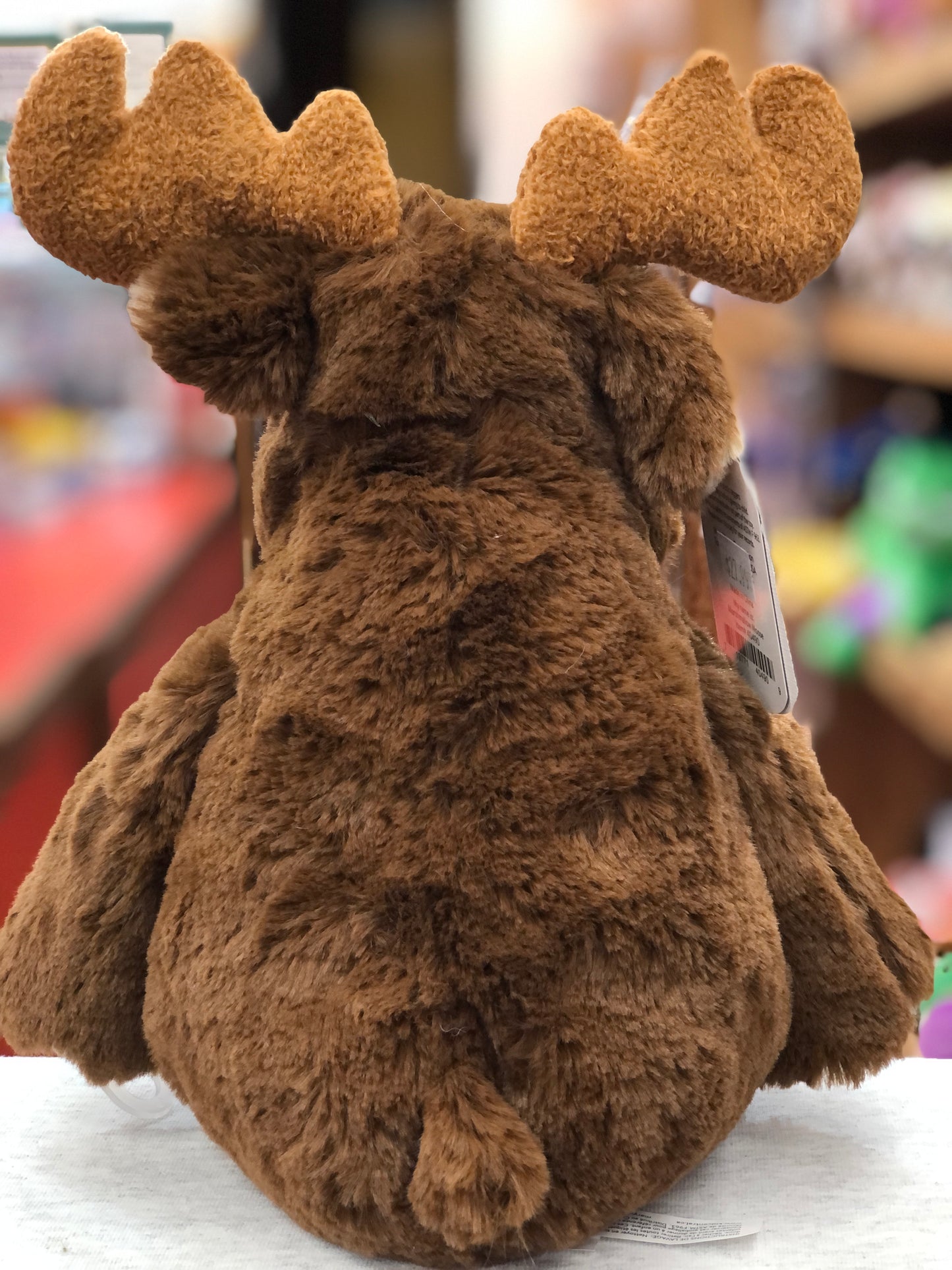 Soft, cuddly Mary Meyer Marshmallow Moose plush toy with large antlers, shown from behind in a store display