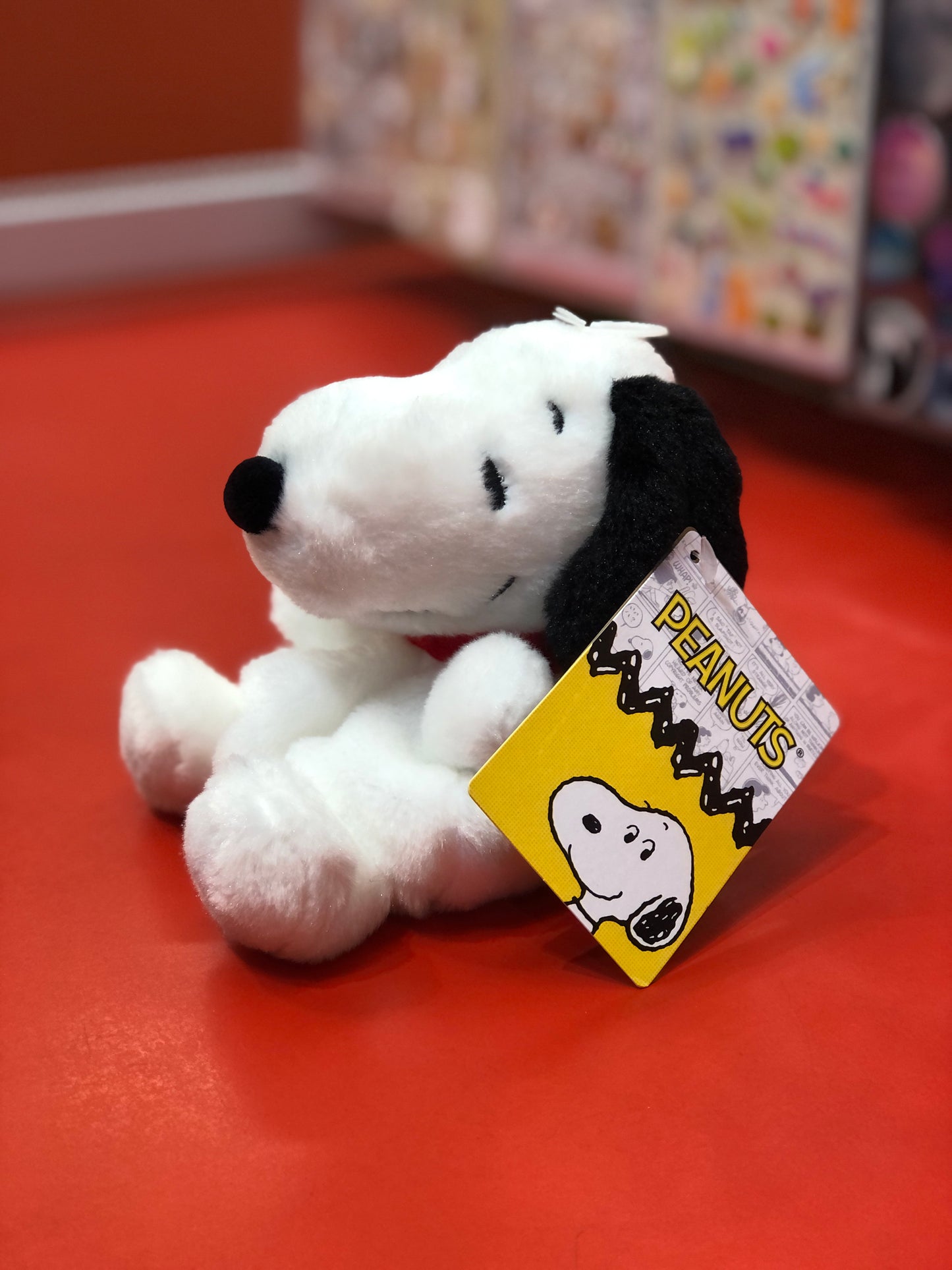 Aurora Peanuts Snoopy plush toy with tag, sitting on red surface, part of Palm Pals collection