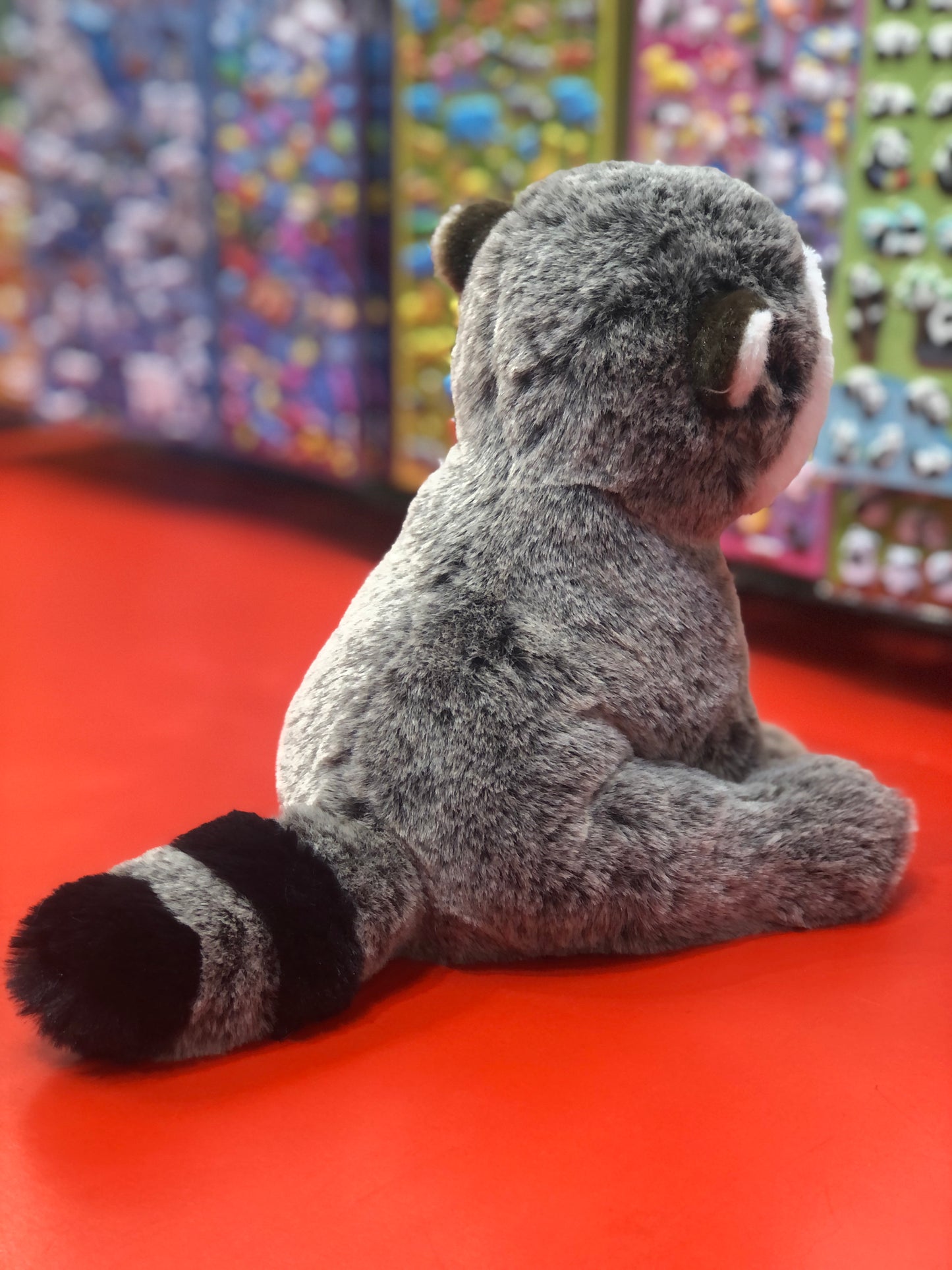 Soft gray Douglas Mini Rudie raccoon plush toy sitting on red surface, showcasing detailed fur and banded tail