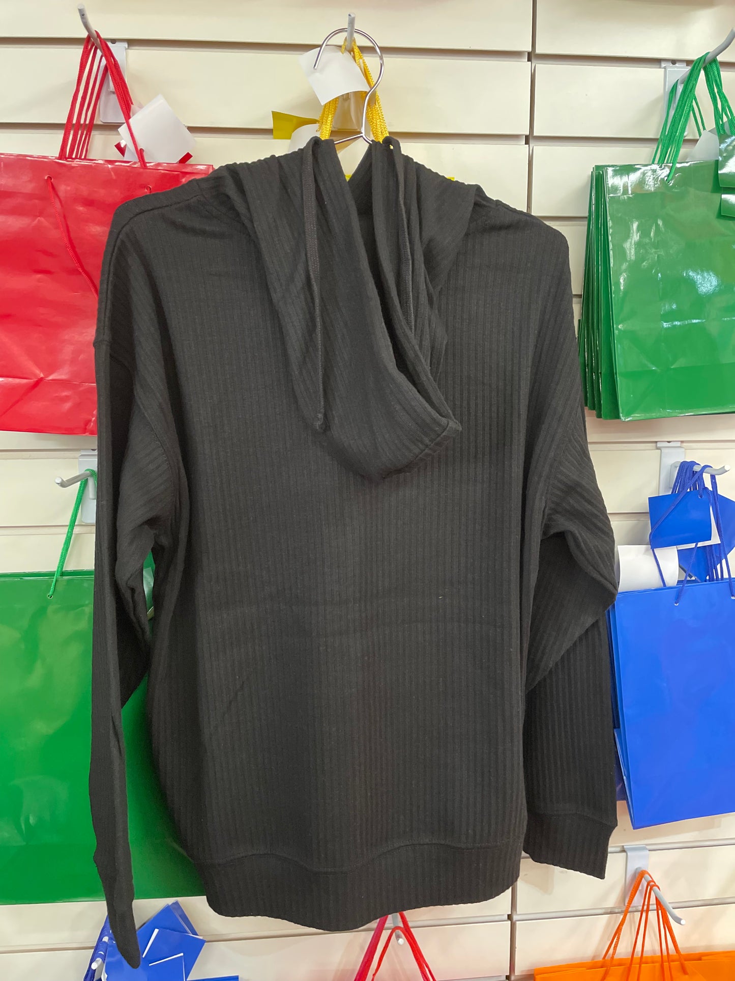 Black ribbed hoody for women displayed on hanger with colorful shopping bags in background