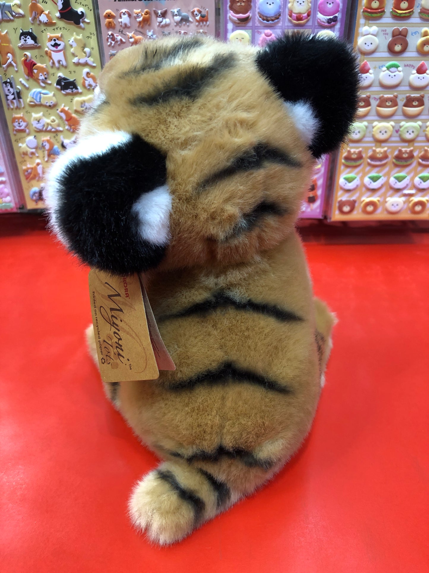 Soft, realistic Aurora Miyoni Bengal Tiger Cub plush toy with striped fur and chubby legs on display against colorful animal stickers