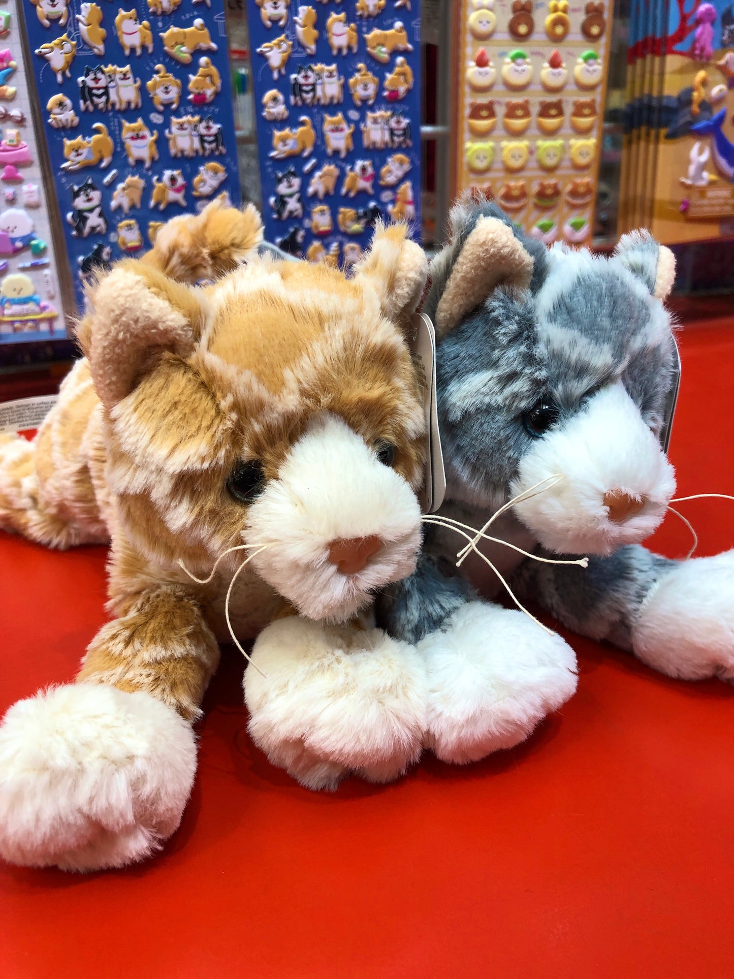 Soft, plush Waffles Kittens in orange and gray, displayed on red surface with colorful animal stickers in background