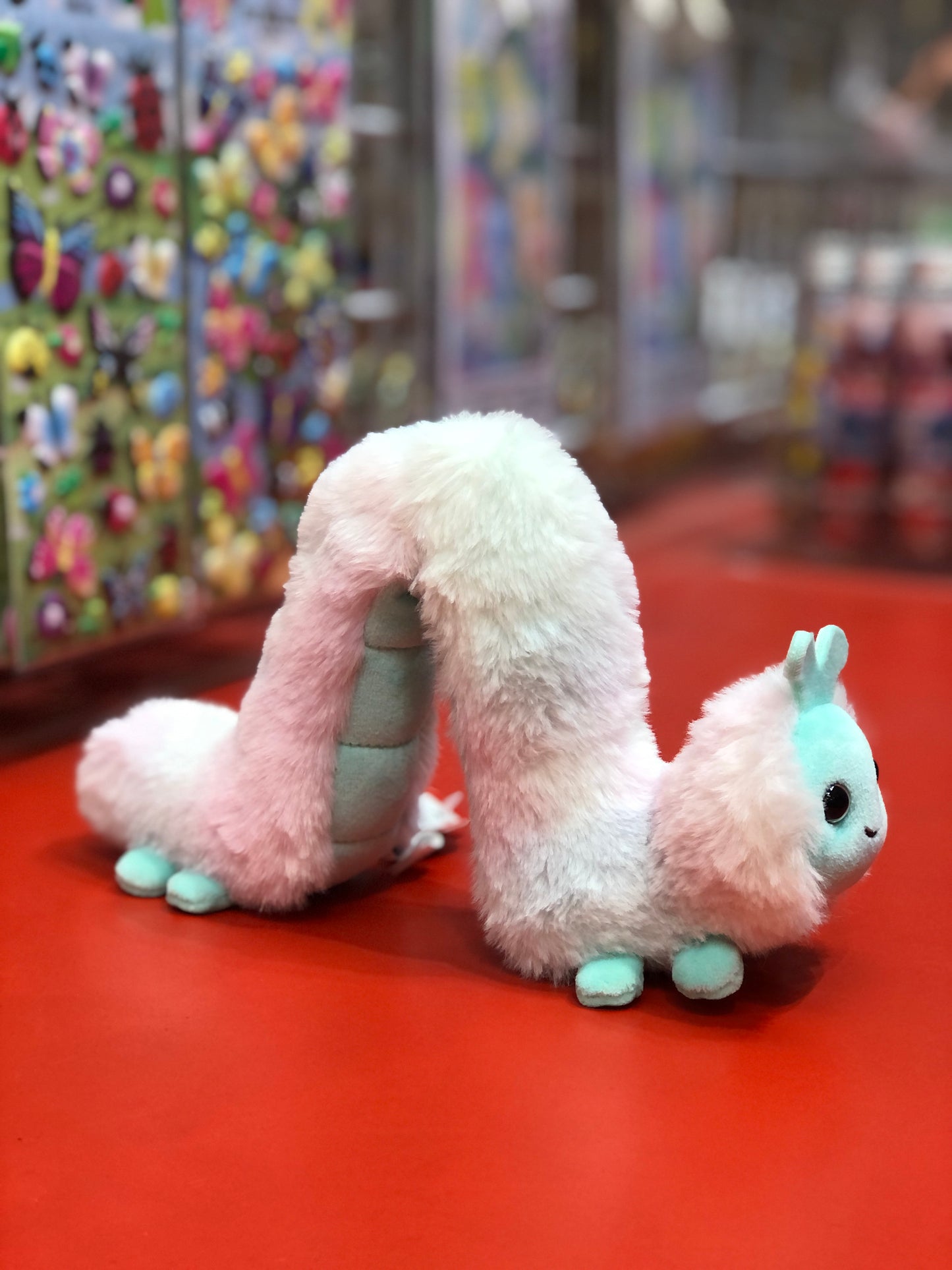 Soft pink and white plush inchworm toy on red display, colorful toy backdrop, vibrant Douglas stuffed animal for kids