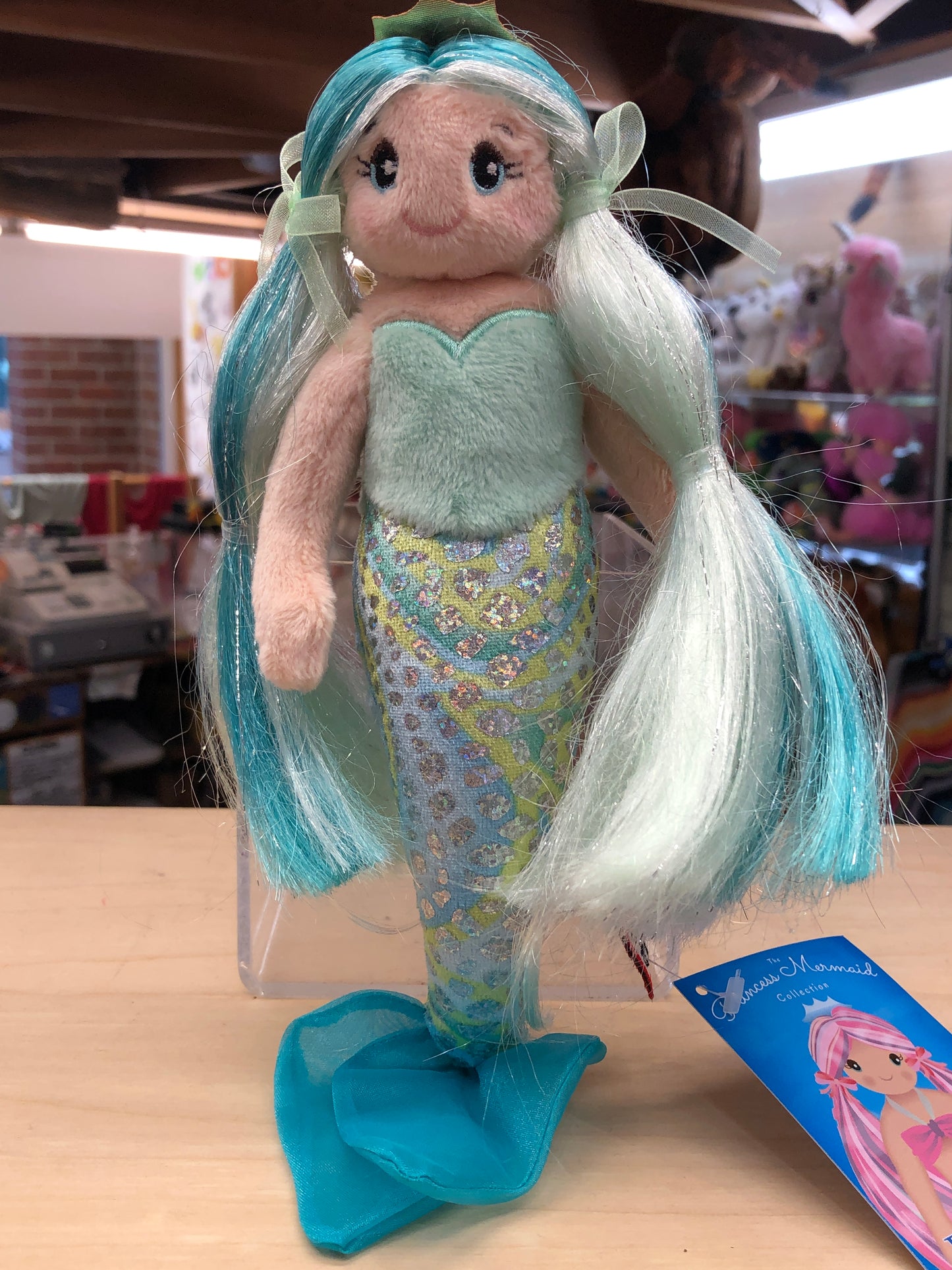 Colorful Douglas Princess Mermaid plush toy with long blue-white hair, sparkling tail, and crown, displayed on wooden surface
