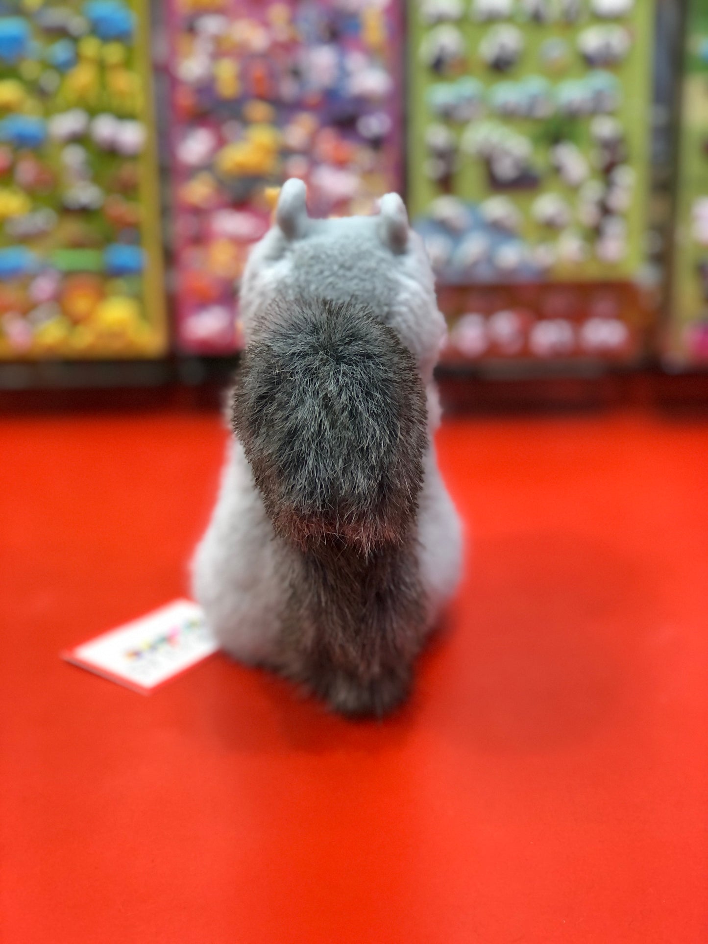 Soft Douglas squirrel plush toy on red display, colorful toy shelves in background, autumn-themed stuffed animal