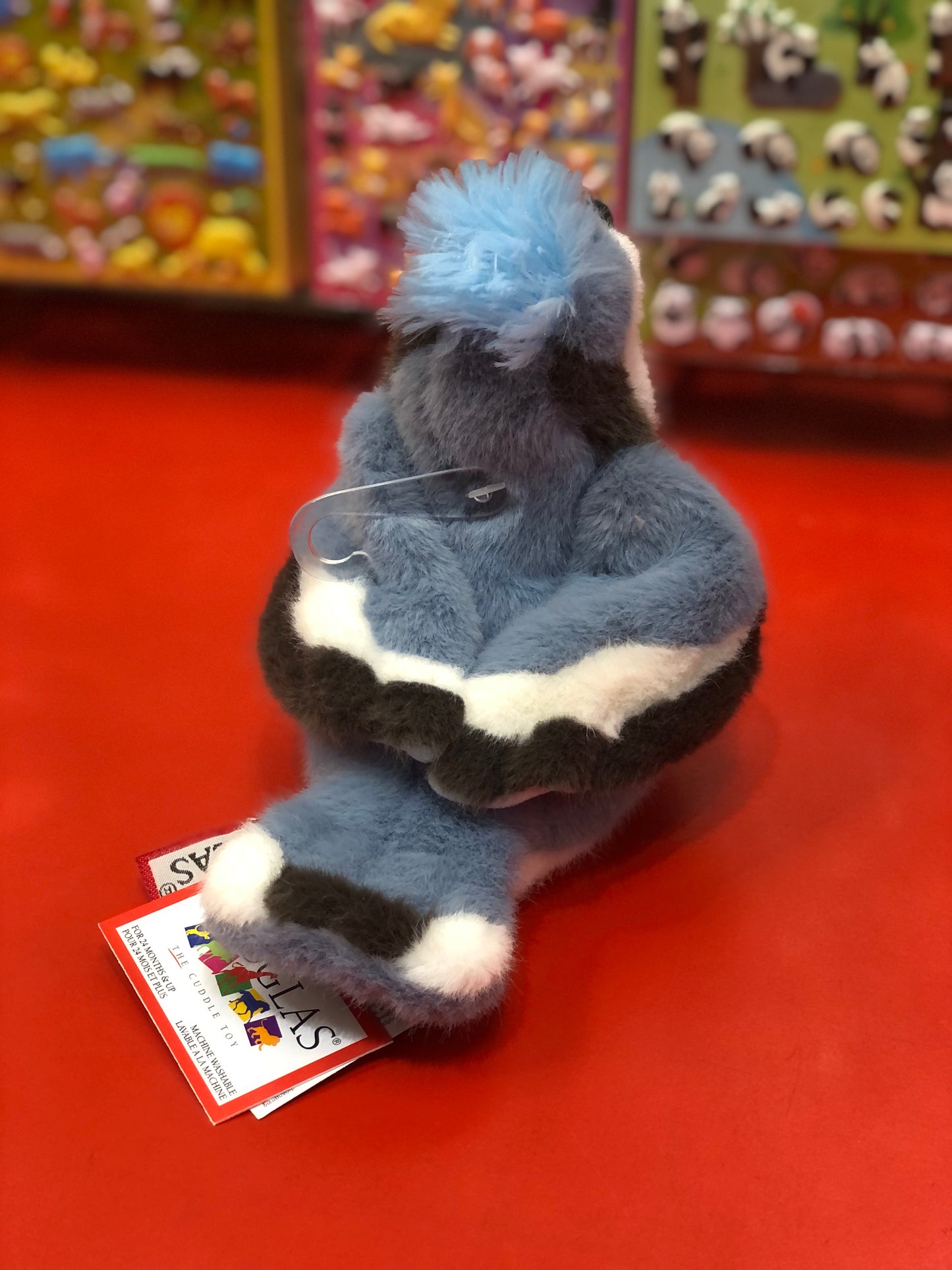 Adorable Douglas denim blue jay plush toy with fluffy crest, sitting on red surface, colorful stuffed animals in background