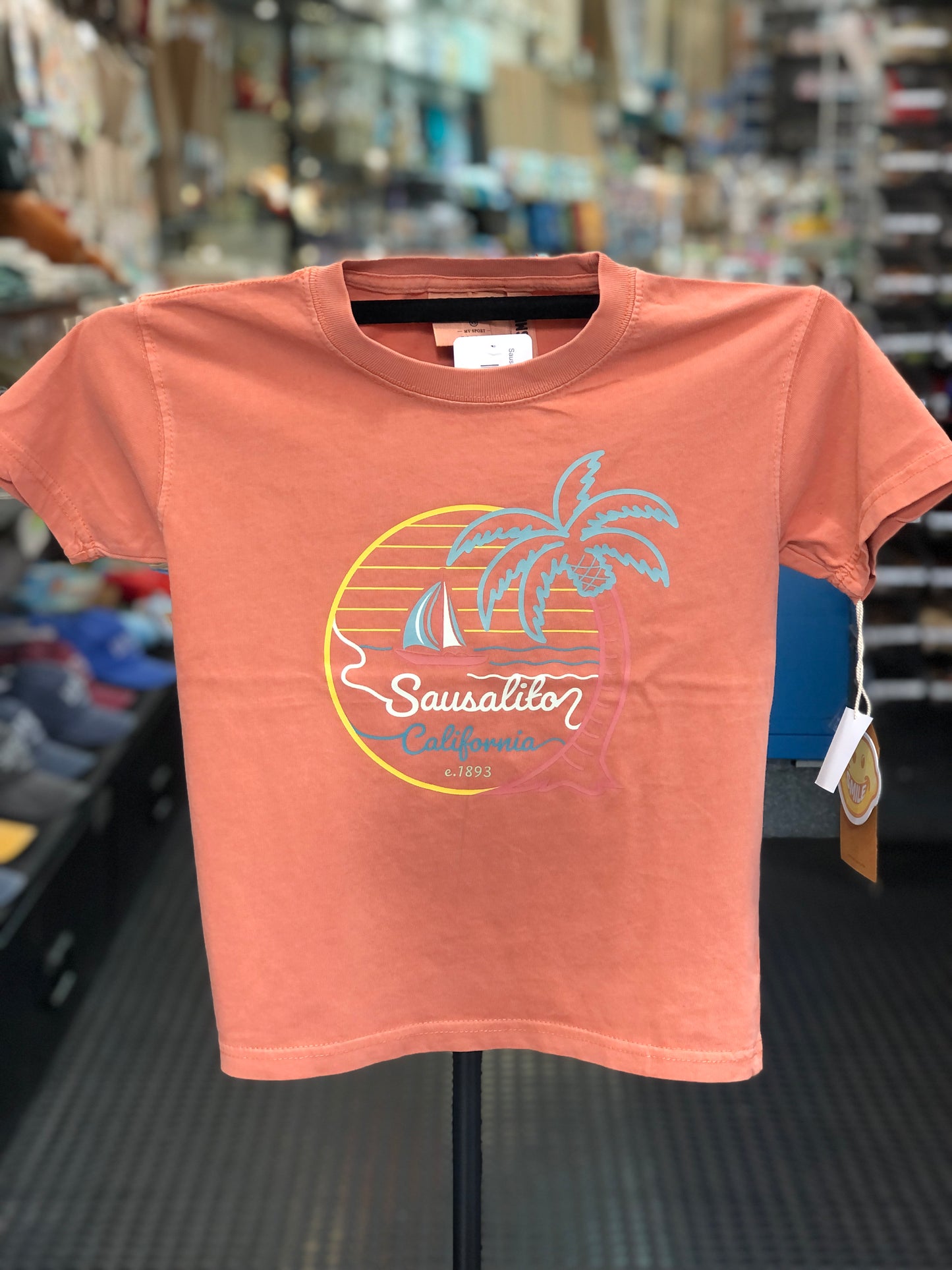 Peach-colored kids t-shirt with a graphic design on a hanger in a store setting.