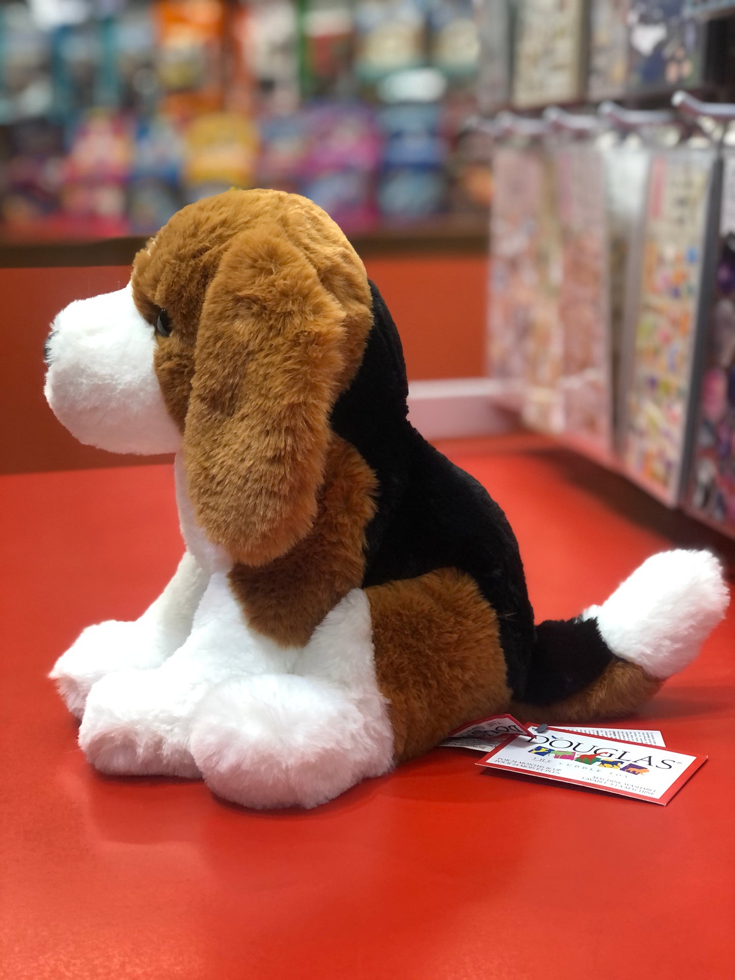 Soft plush Beagle puppy toy, Earnie, sitting on red surface with tag, colorful background, 11-inch cuddly Douglas stuffed animal