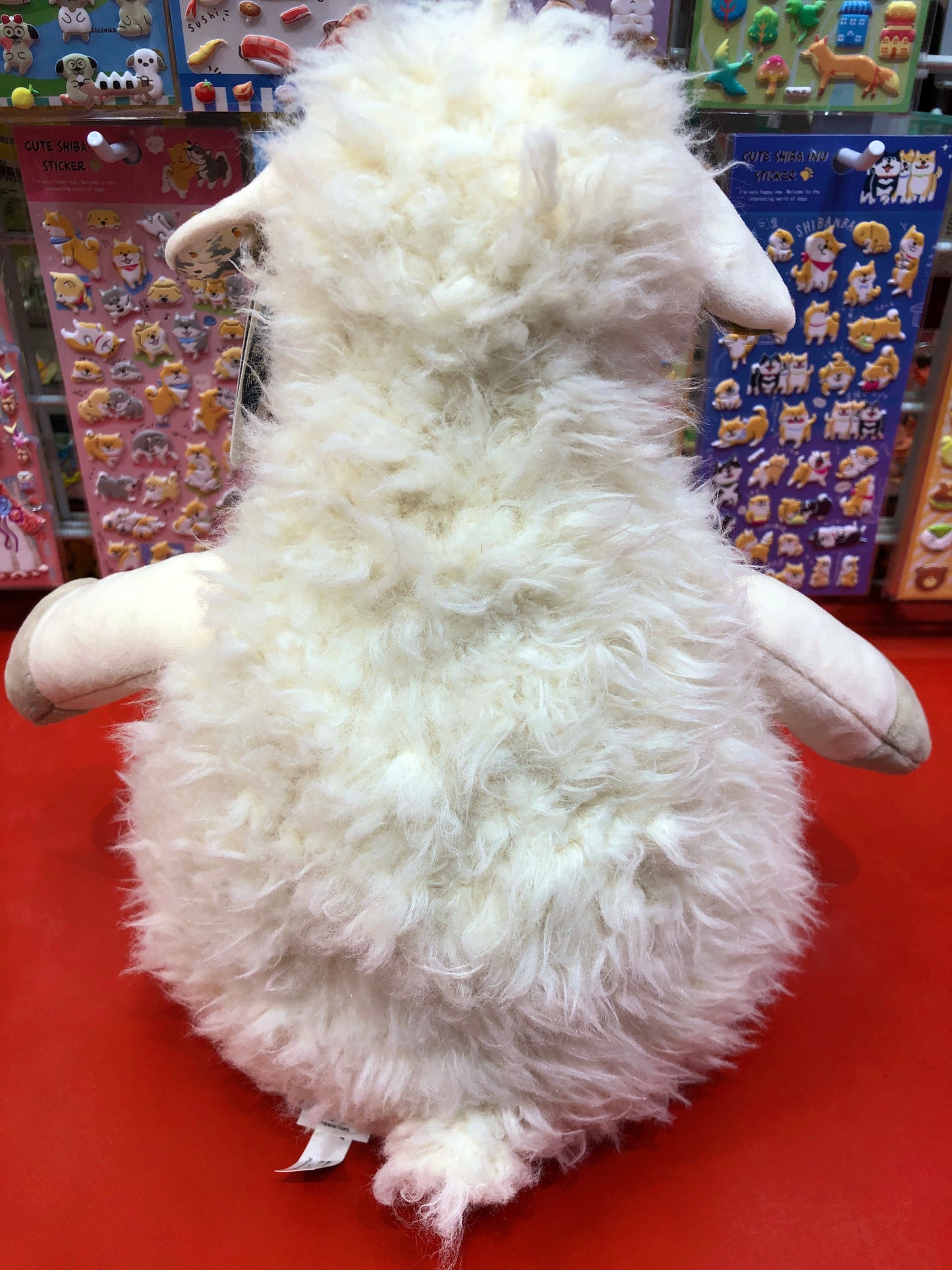 Fluffy white Mary Meyer FabFuzz Nellie Sheep plush toy on red display, surrounded by colorful animal stickers
