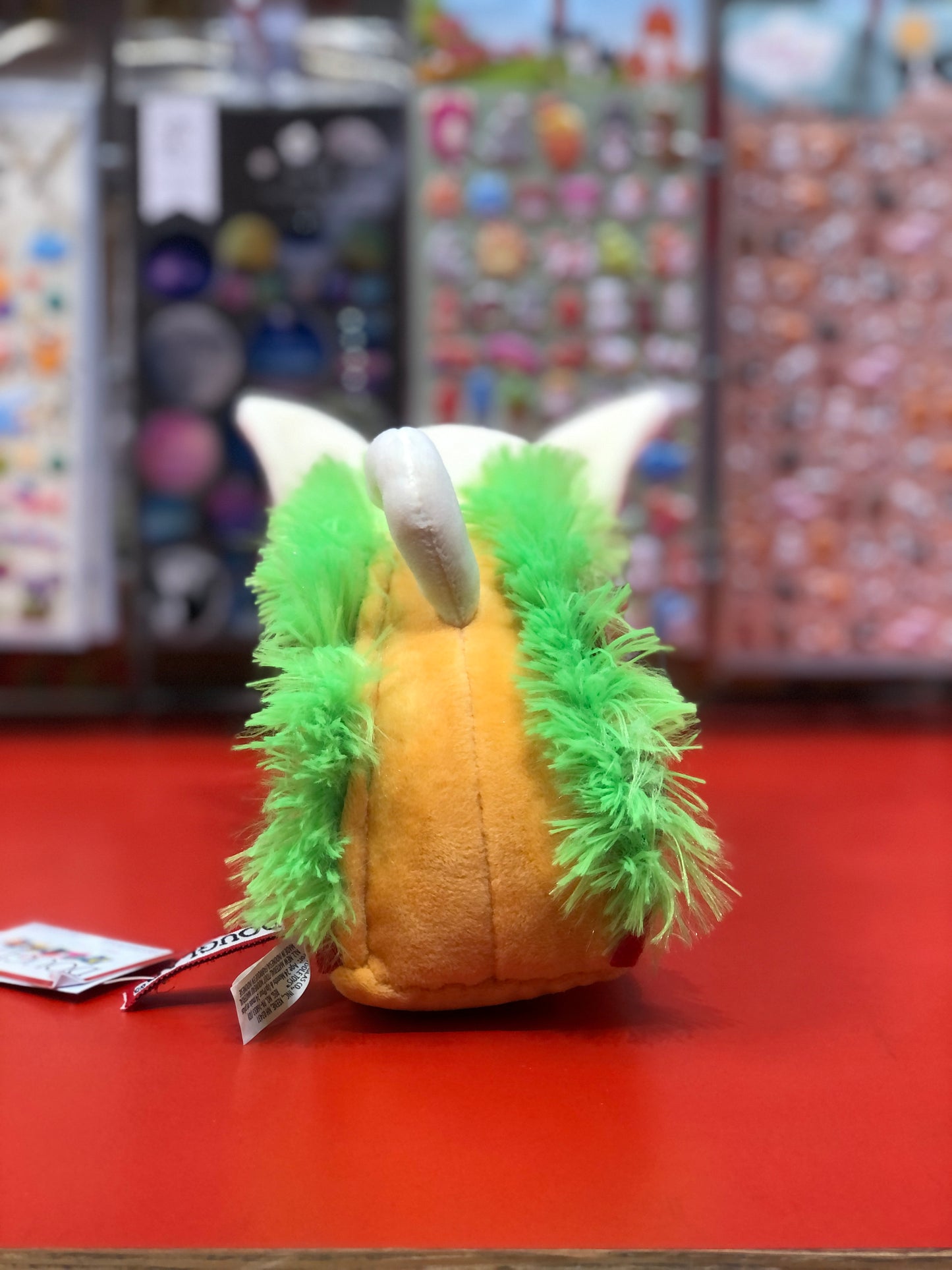 Cute plush Chihuahua dog in taco costume with yellow shell, green lettuce trim, and white ears on red display shelf