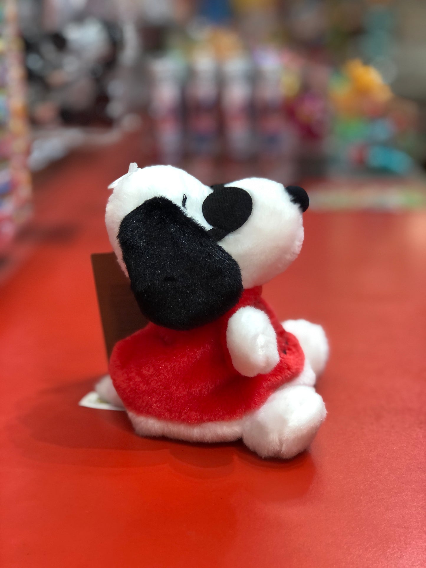 Aurora Peanuts Joe Cool plush toy, featuring Snoopy in red outfit and sunglasses, sitting on red surface