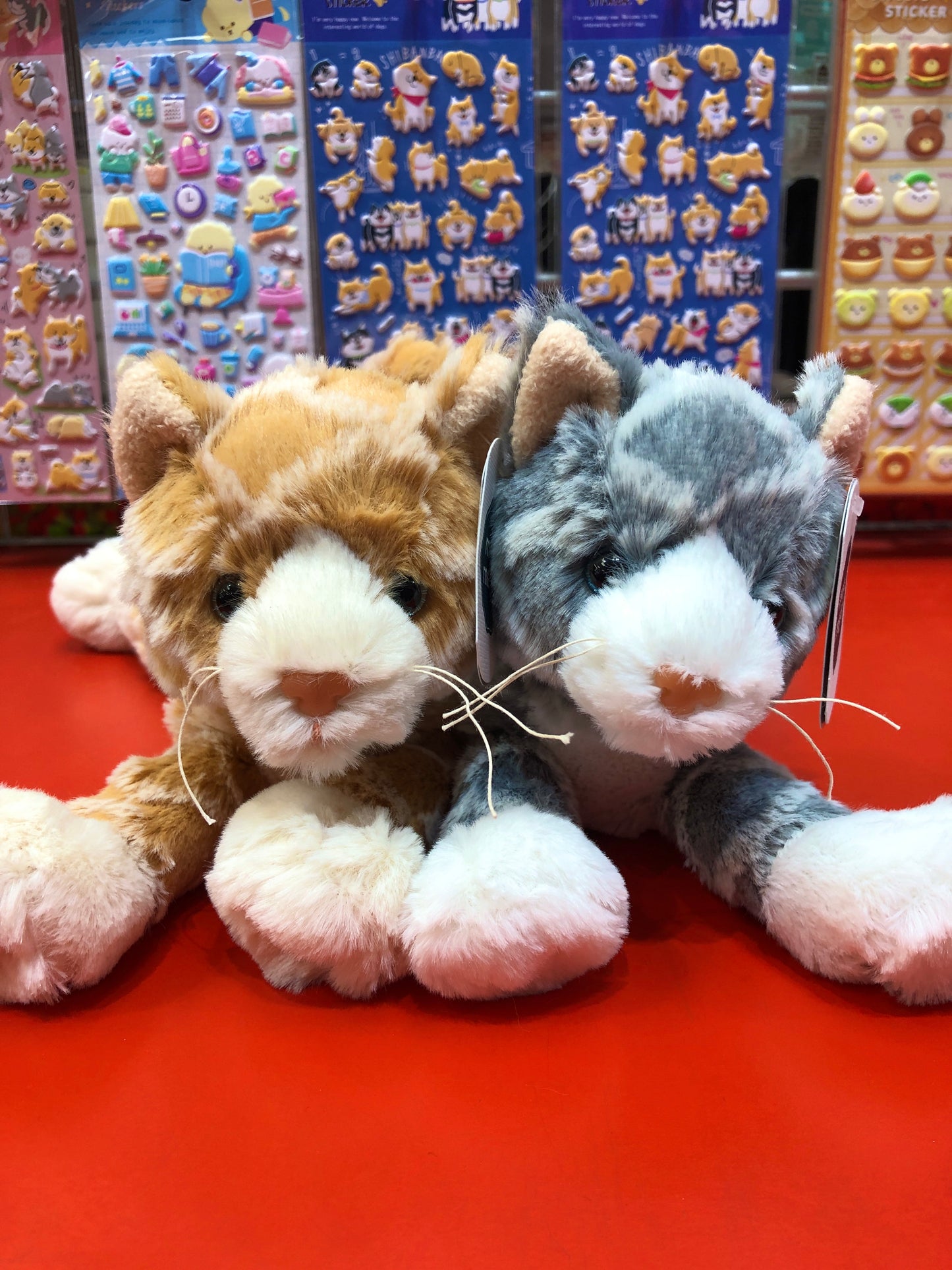 Soft, plush FabFuzz Waffles Kittens in orange and gray, displayed on red surface with colorful sticker sheets in background