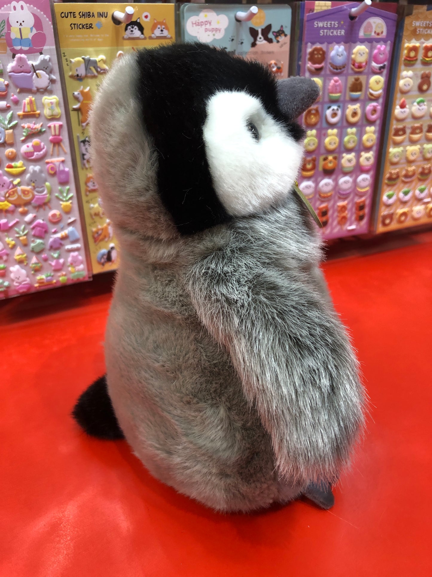 Fluffy Emperor Penguin chick plush toy with realistic gray feathers and black-white markings, displayed near colorful stickers