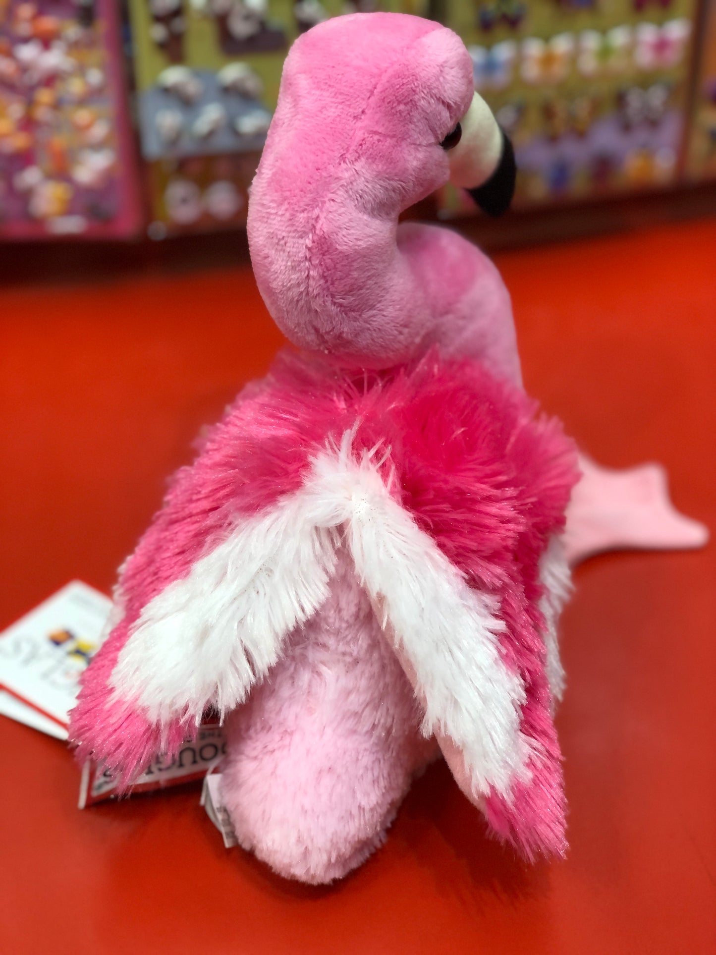 Soft pink flamingo plush toy with curved neck, black beak, and fluffy feather-like texture on a red surface