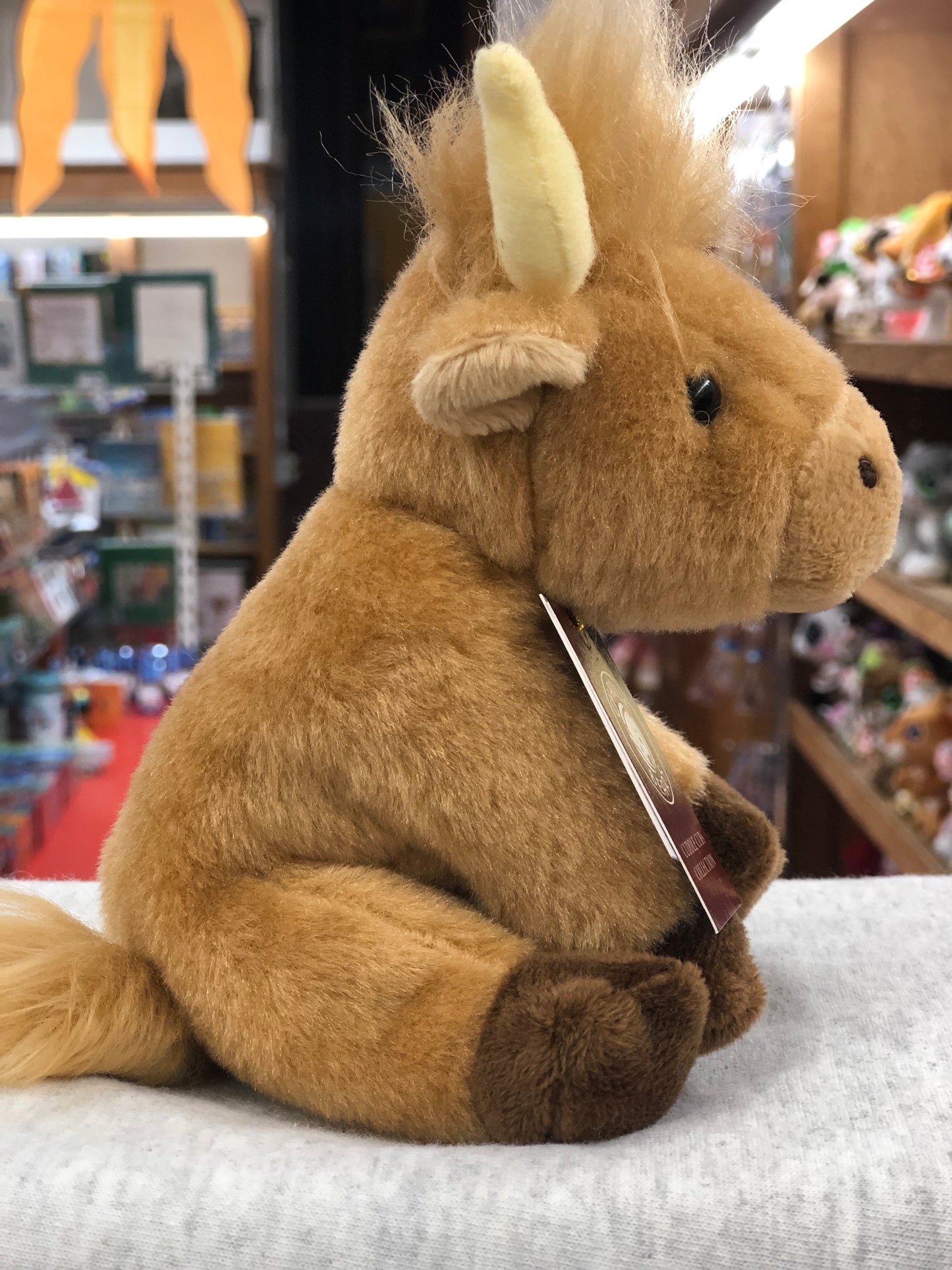 Soft, cuddly Charlie Bears Highland Cow plush toy for babies, shown in store display with fluffy fur and distinctive horns