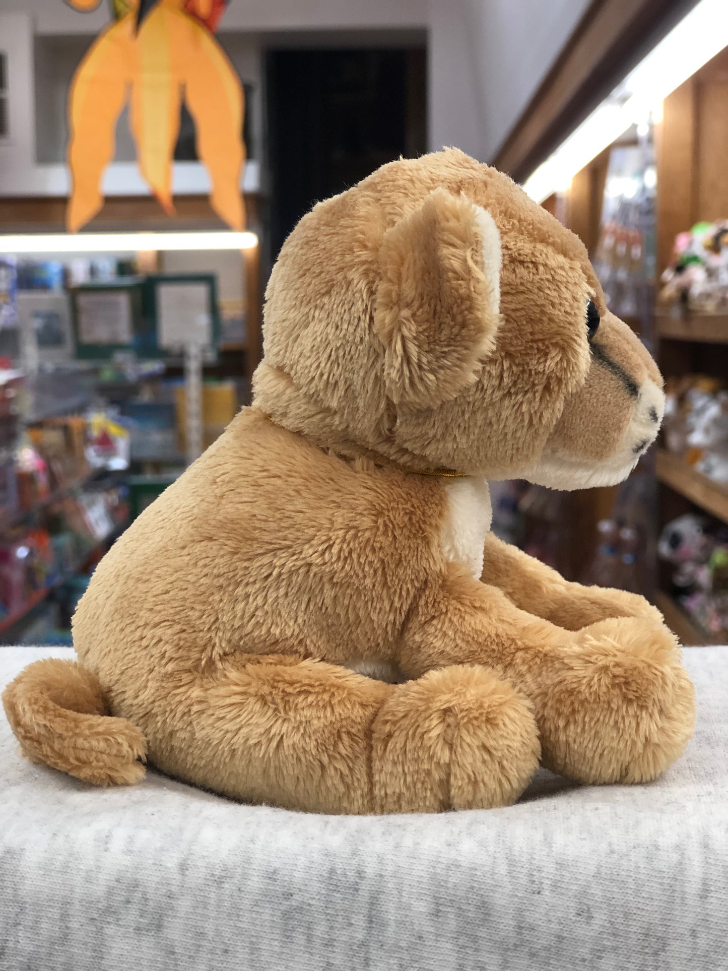 Soft, plush Charlie Bears Cuddle Cub Lioness sitting in toy store, perfect size for baby hands, featuring tan fur and cute profile