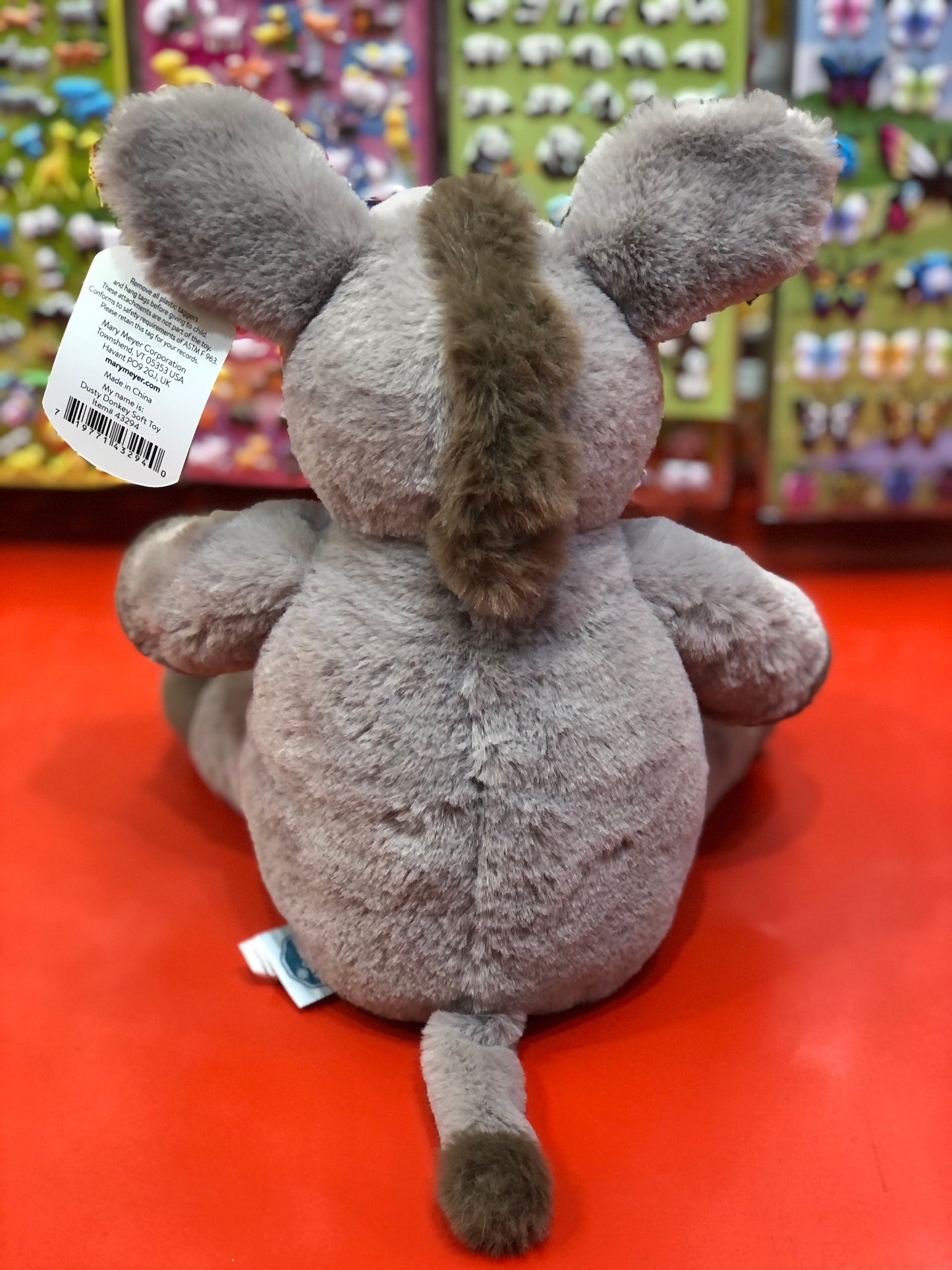 Soft plush donkey toy with large ears and fluffy mane, displayed on red surface in toy store setting