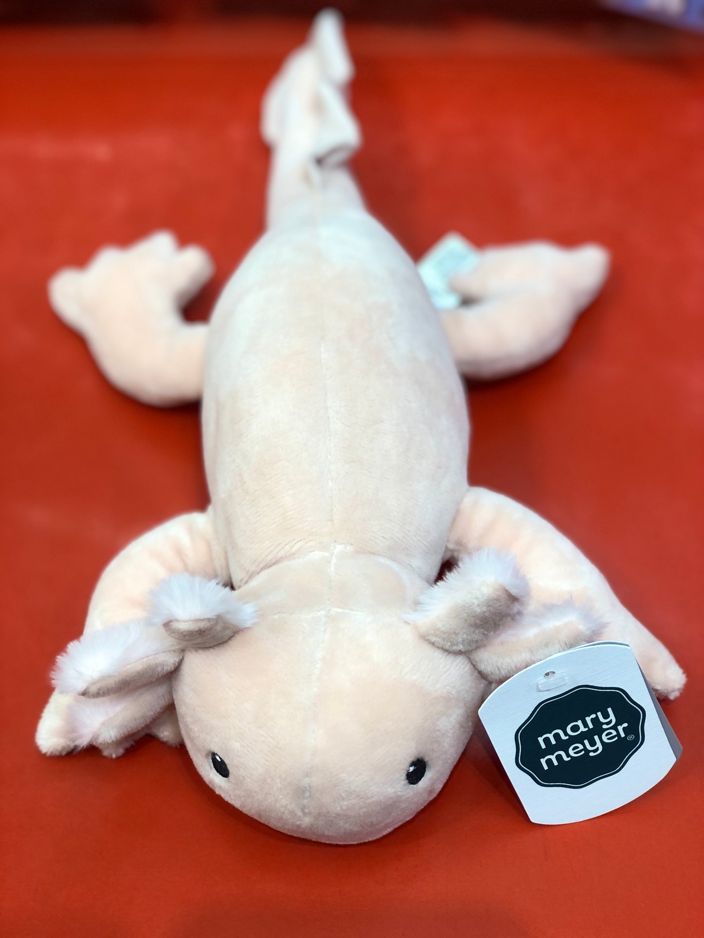 Soft white Izzy Axolotl plush toy by Mary Meyer, featuring embroidered eyes and grin, on red background