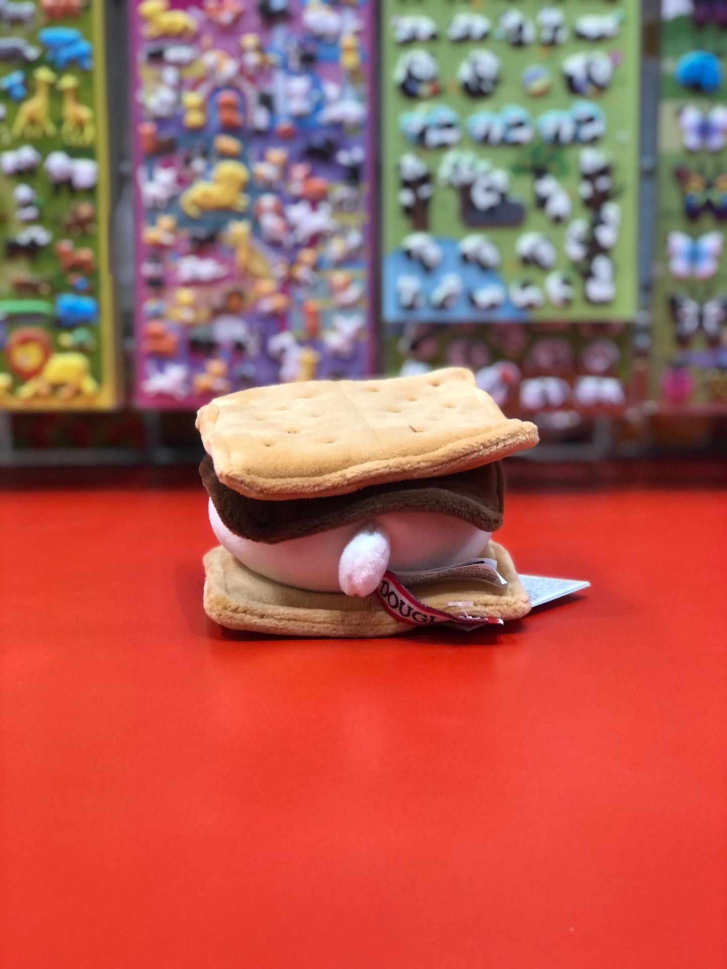 Cute s'more bear plush toy on red display, realistic graham cracker and chocolate design, colorful toy shelves background